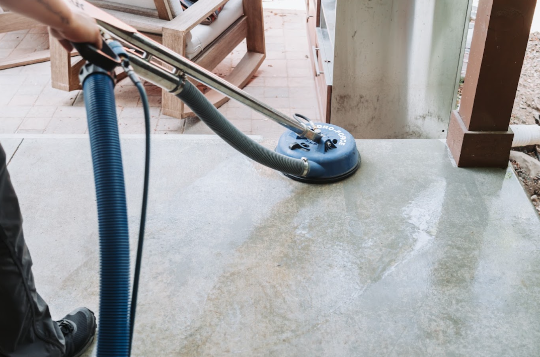 Blue vacuum hose cleaning a wet concrete floor near a doorway.