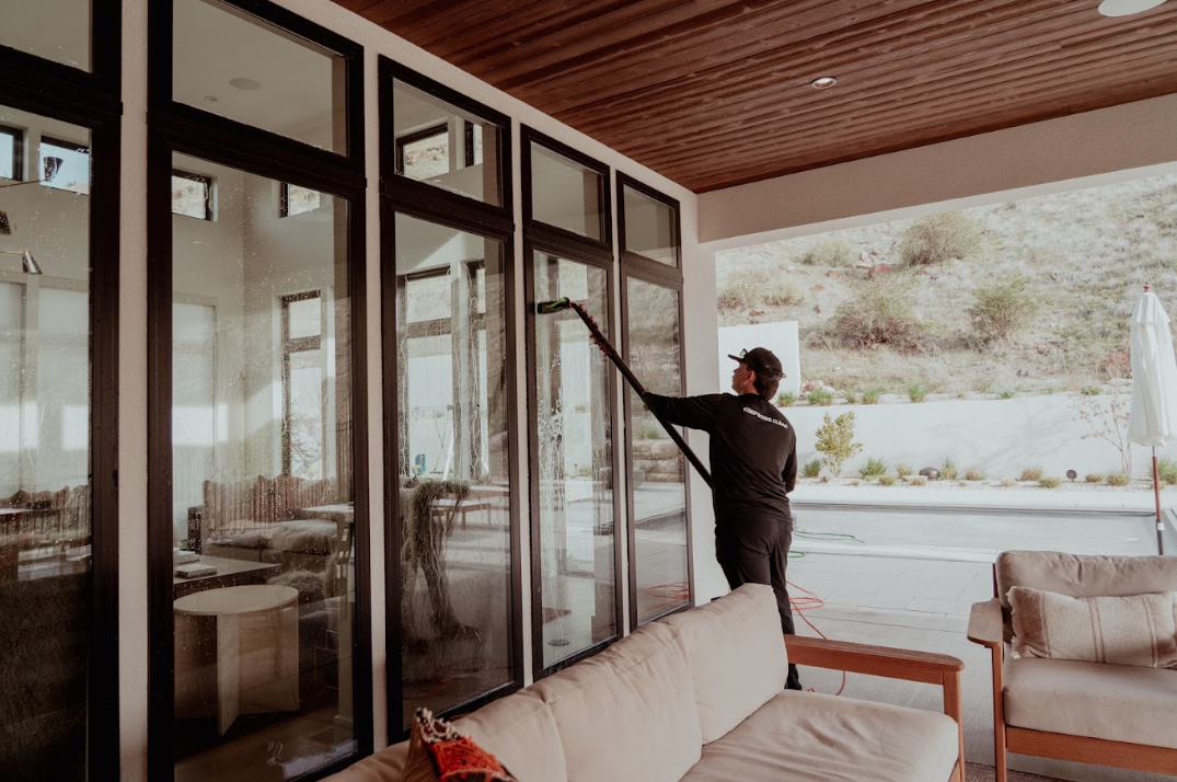 Person cleaning tall glass doors on a patio with outdoor seating and mountains in the background