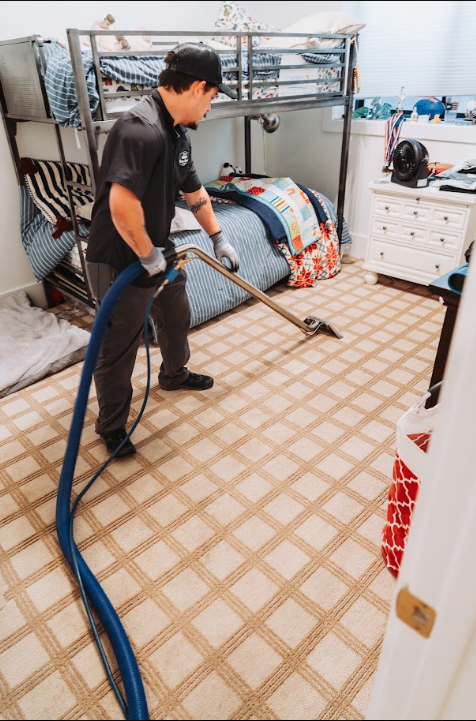 Worker using a steam cleaner on a carpeted floor beside a bunk bed and dresser