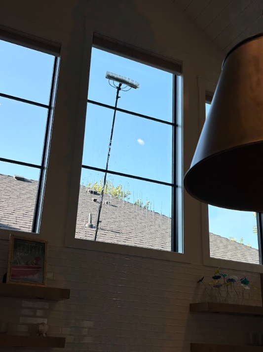 Sunlit room with tall windows, blue sky, rooftops outside, and a large lampshade in the foreground
