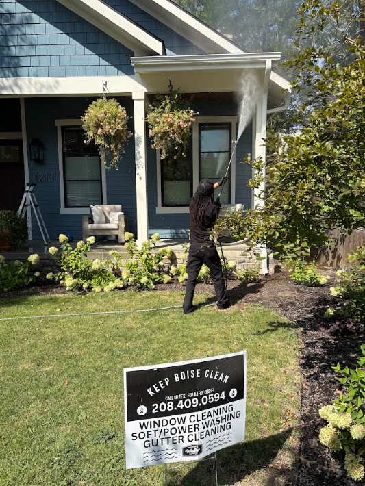 Person in black walking on a lawn in front of a blue house with a porch sign.