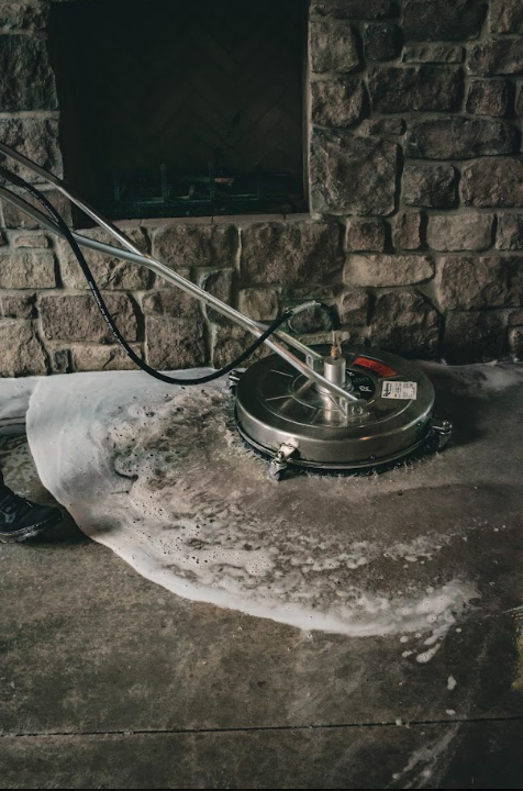 Floor buffer cleaning a wet concrete floor near a stone wall