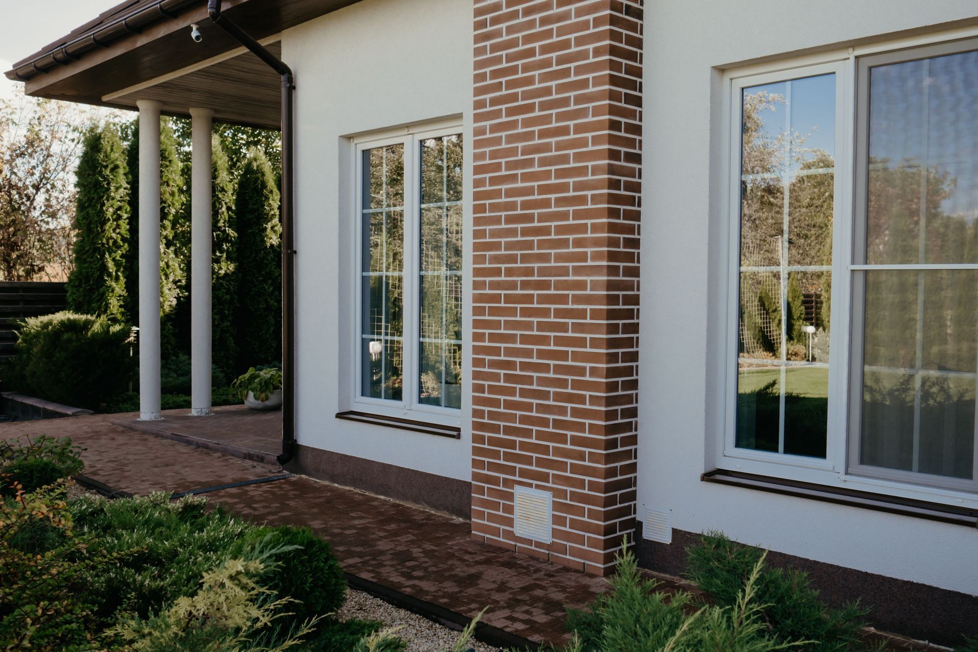 Brick house exterior with white-trimmed French doors, covered porch, and landscaped yard