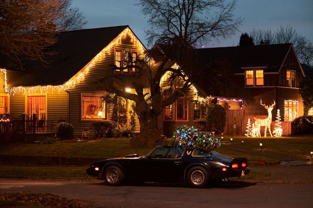 House decorated with warm Christmas lights at night, with a car parked in front.