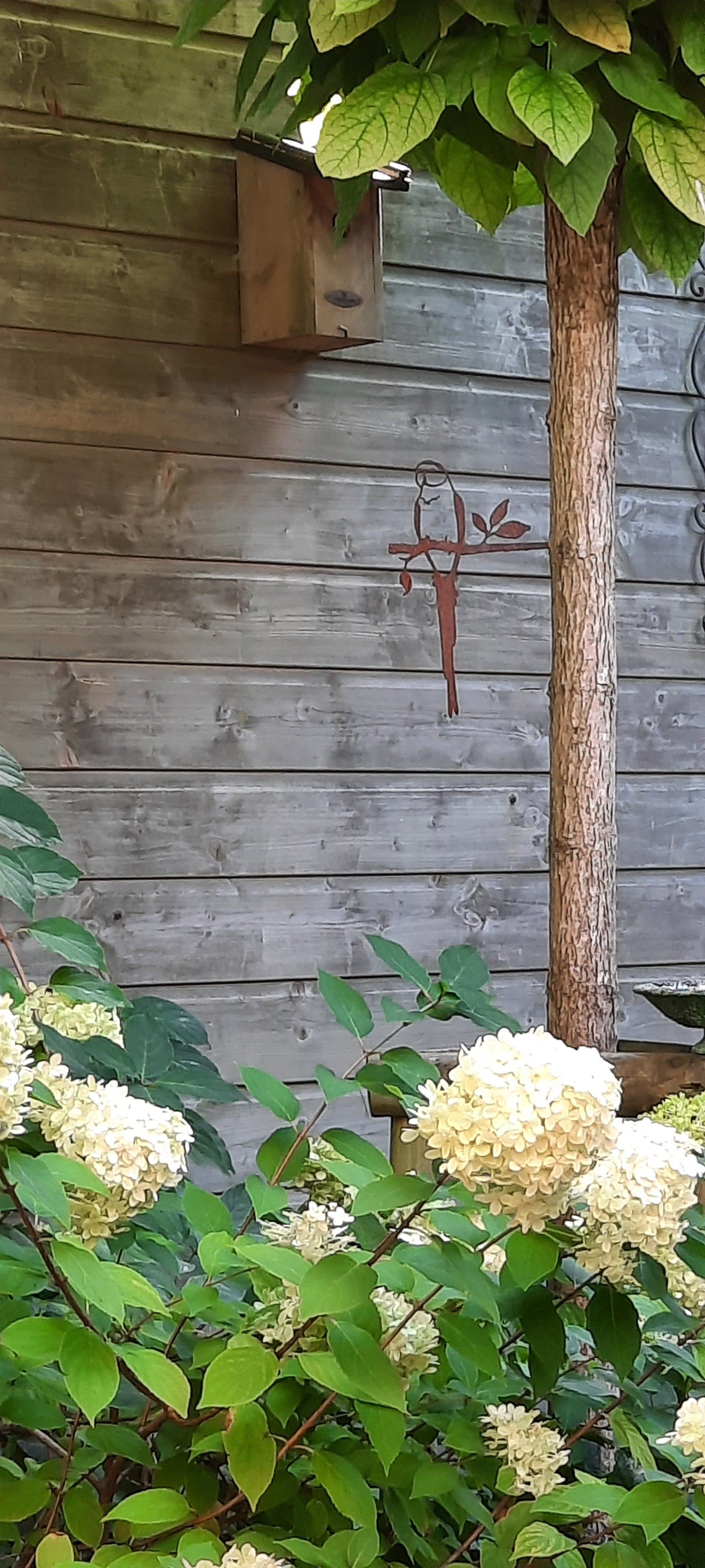 Een houten muur met een hangend kruis en bloemen ervoor.