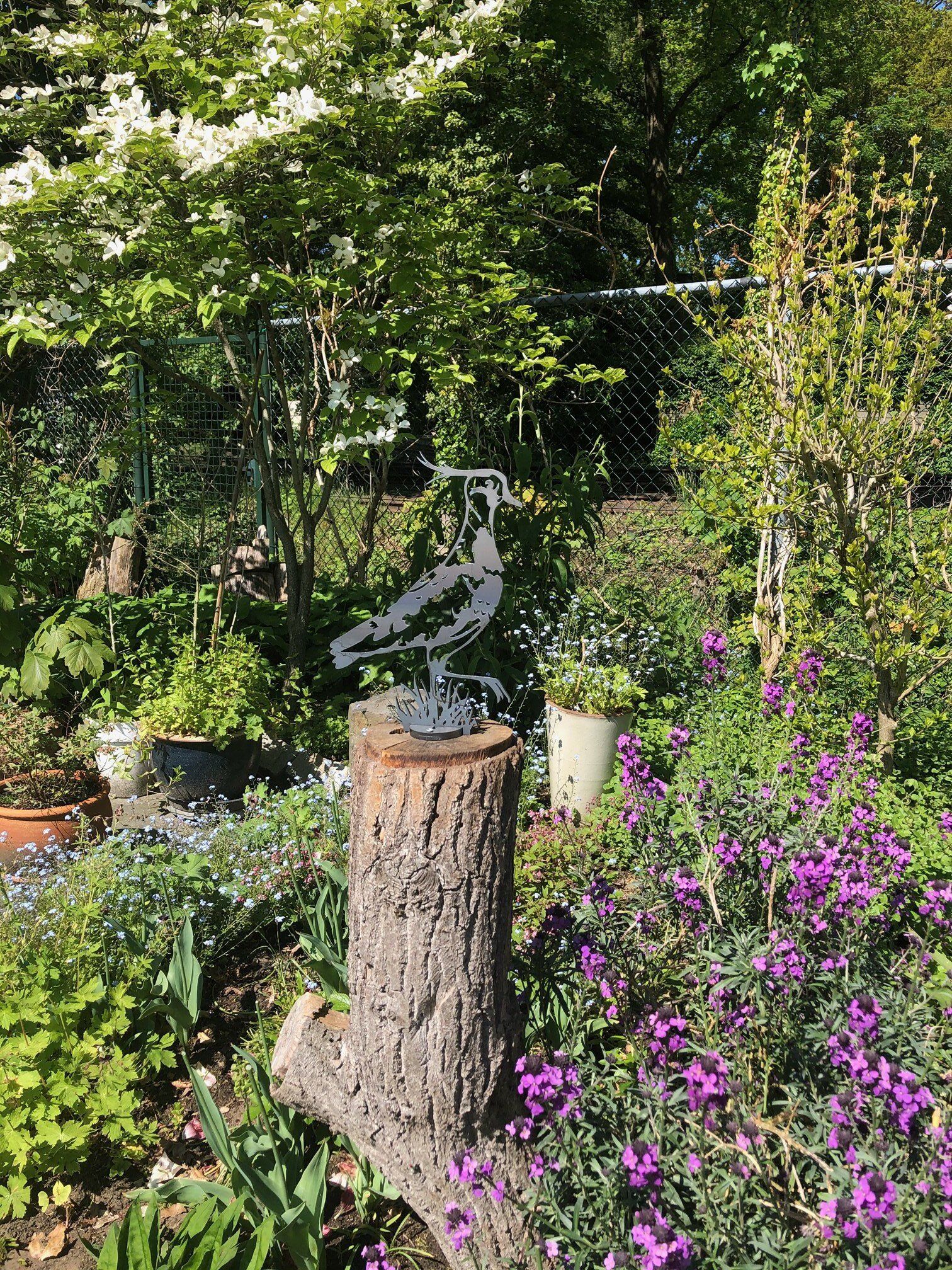 Er staat een standbeeld van een vogel op een boomstronk in het midden van een tuin.