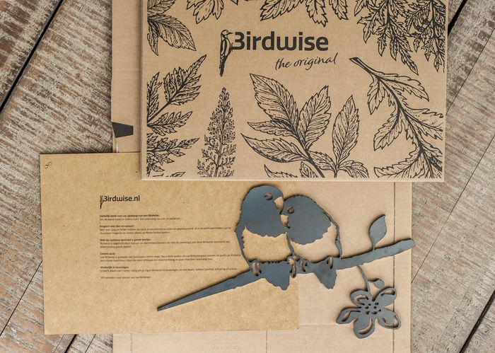 Lasergesneden vogelkunst op een achtergrond van kraftpapier. De kunst toont twee vogels op een tak en een bloemenversiering.