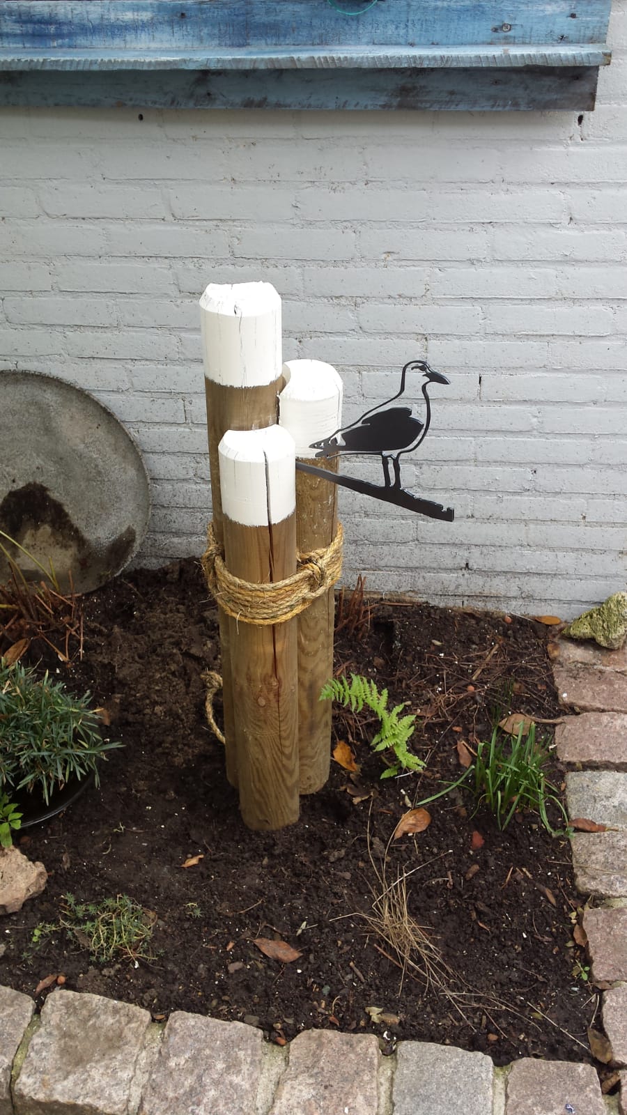Een meeuw zit op een houten paal in een tuin.