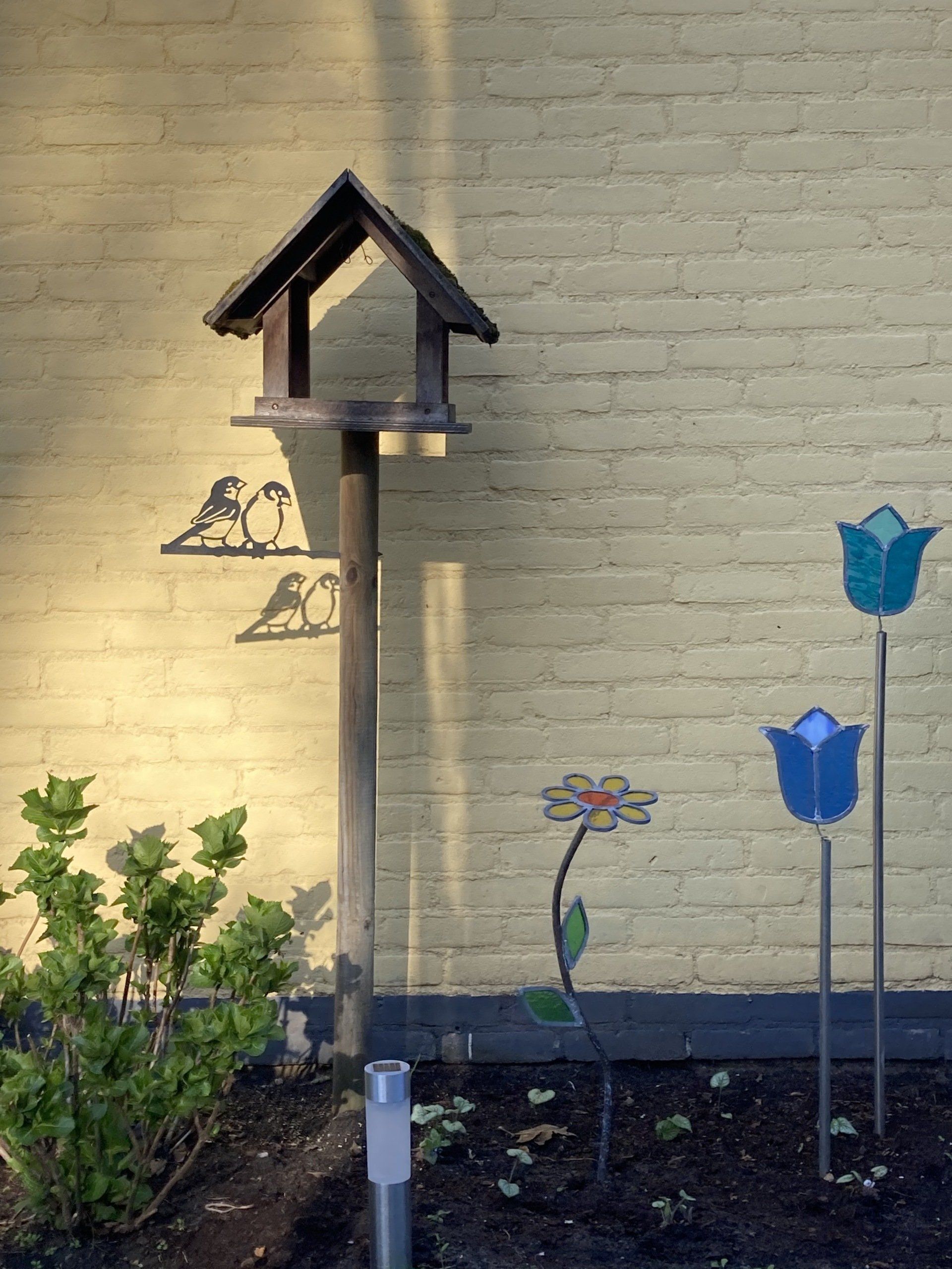 Een vogelhuisje staat voor een gele bakstenen muur