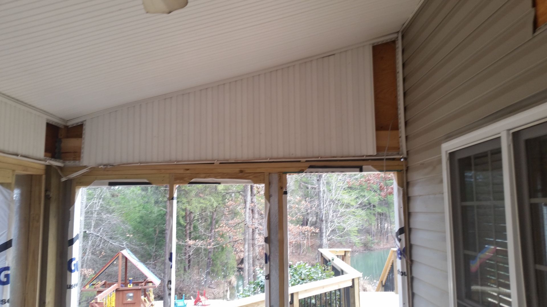 Sunroom with exposed framing, white paneling, and sliding glass doors overlooking a wooded area.