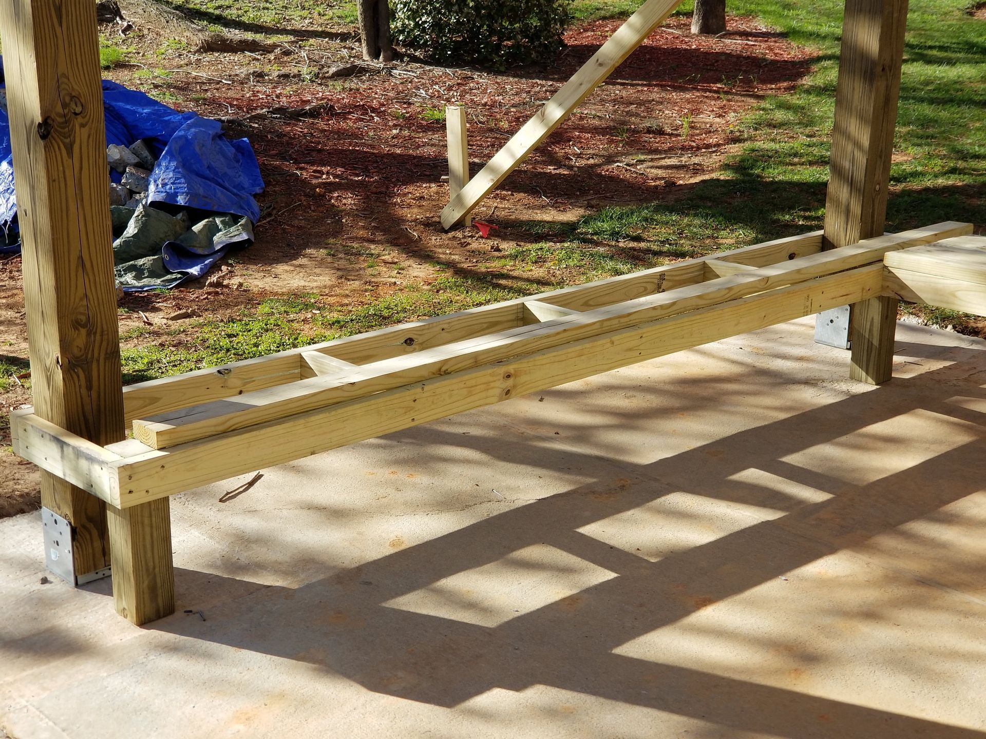 Wooden frame of a structure under construction, supported by posts on a concrete surface.