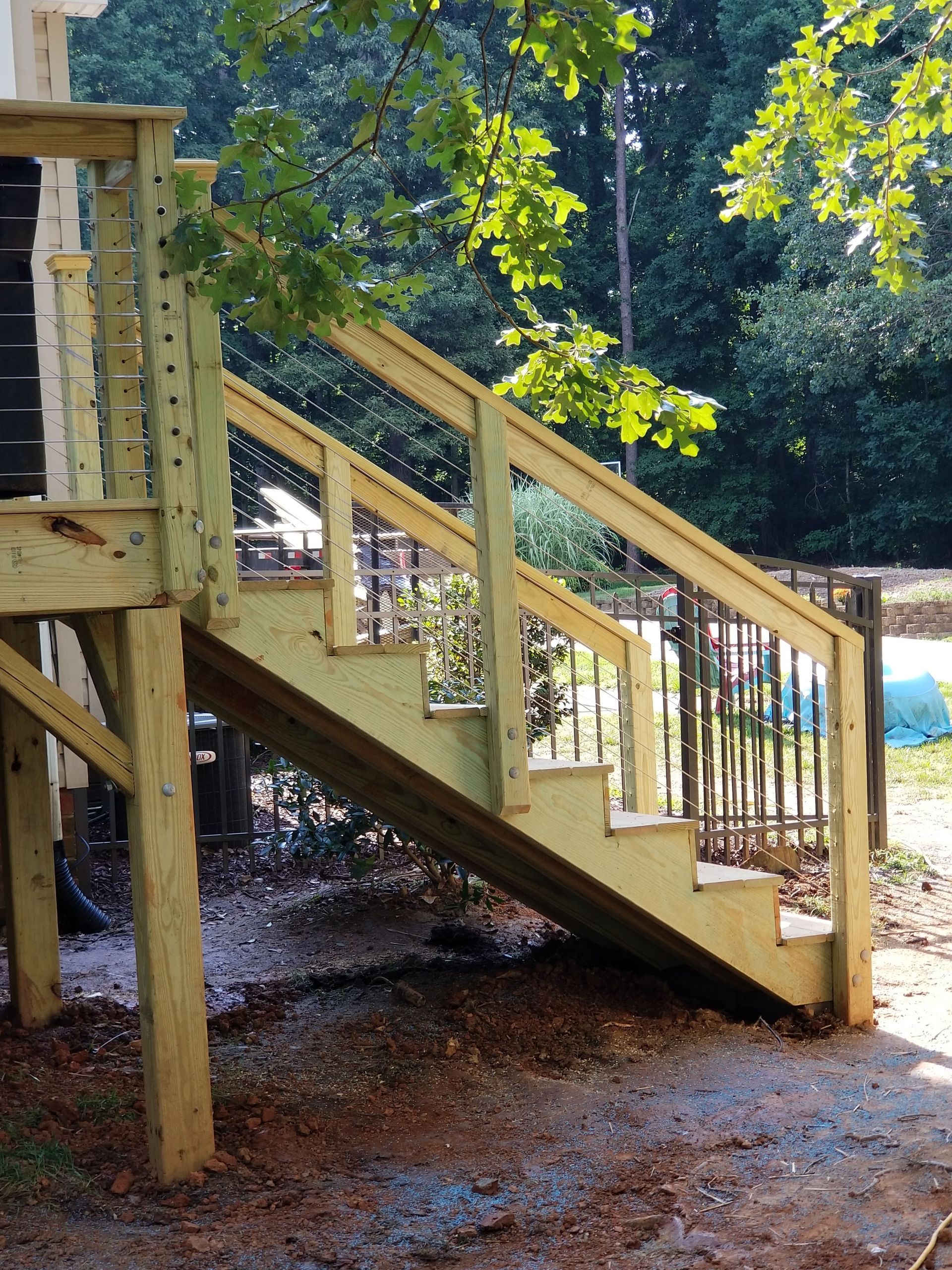 Wooden deck stairs with railings leading down, surrounded by trees.