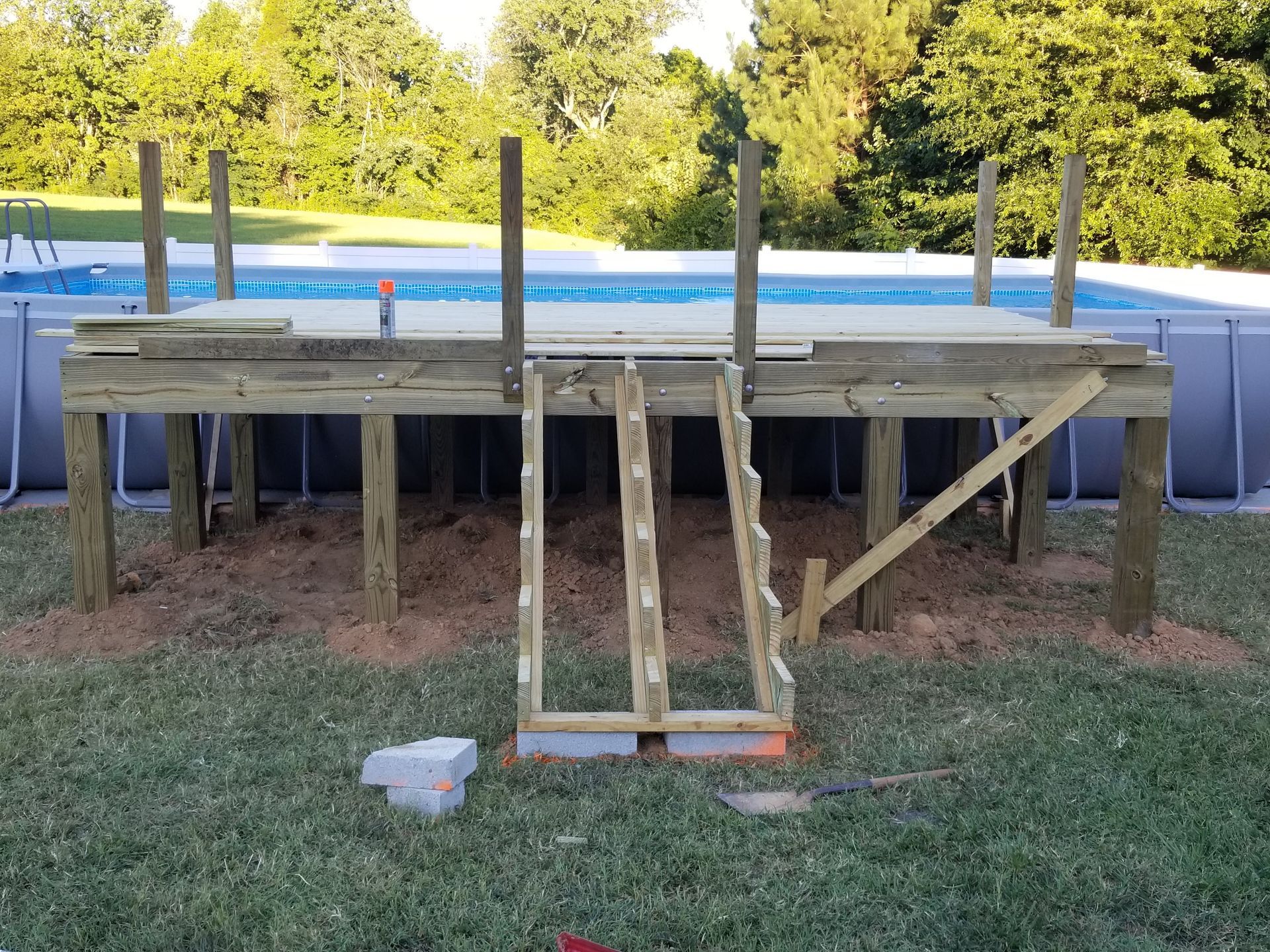 Partially built wooden deck with ladder for an above-ground pool, on grass.