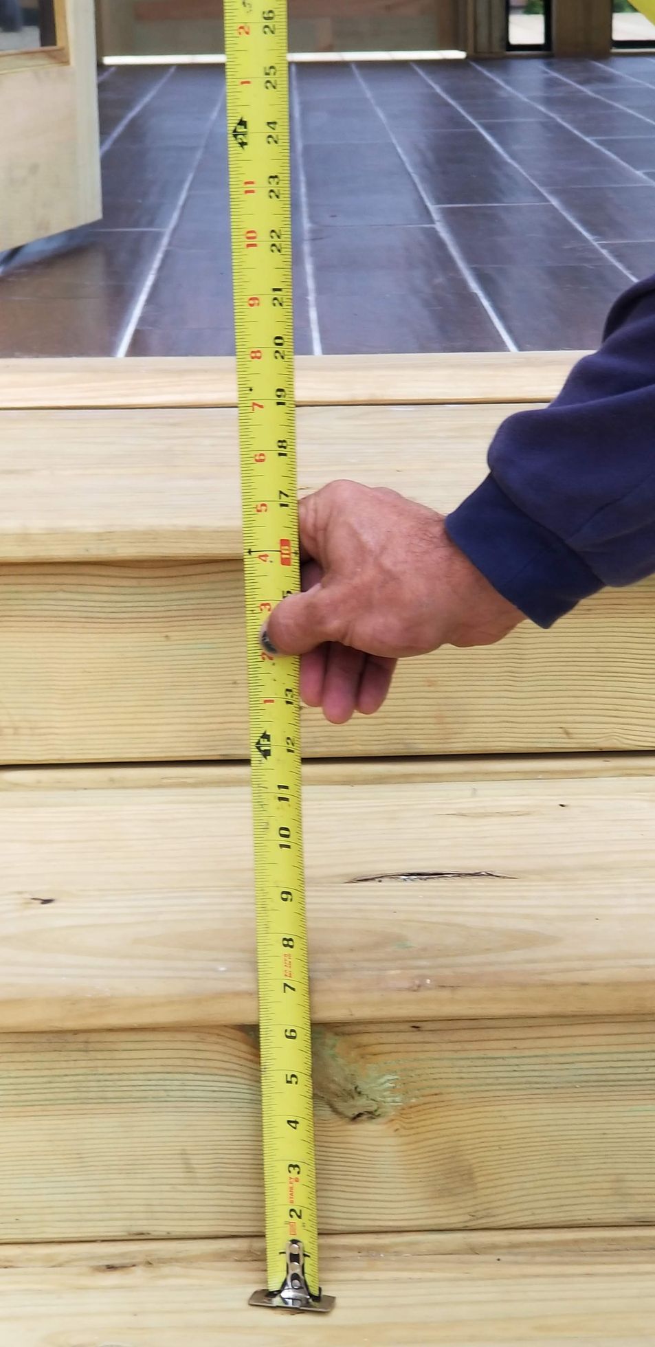 Person measures wooden steps with a yellow tape measure, outdoors.