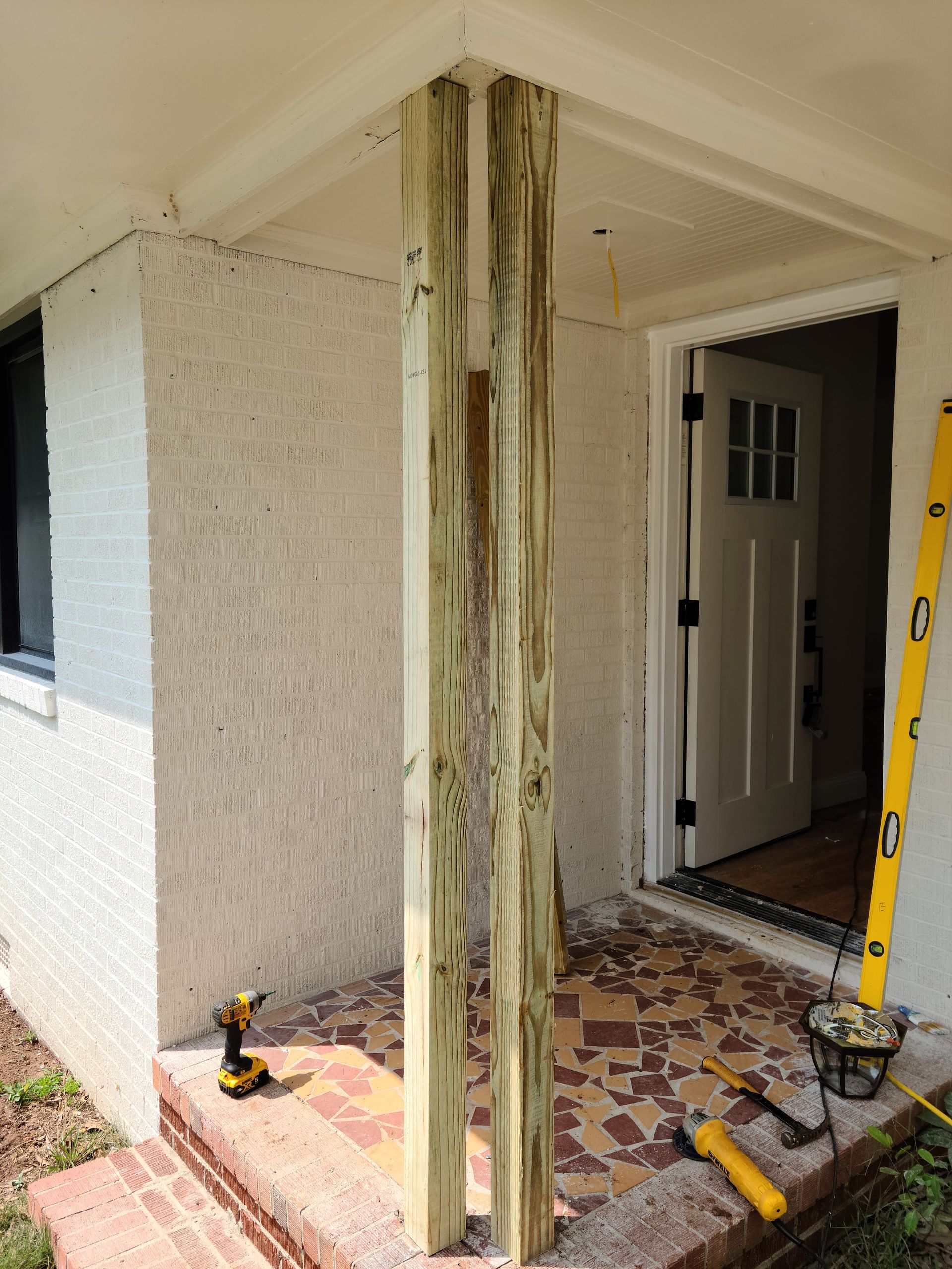 Wooden posts being installed on a porch. A drill and level are present.