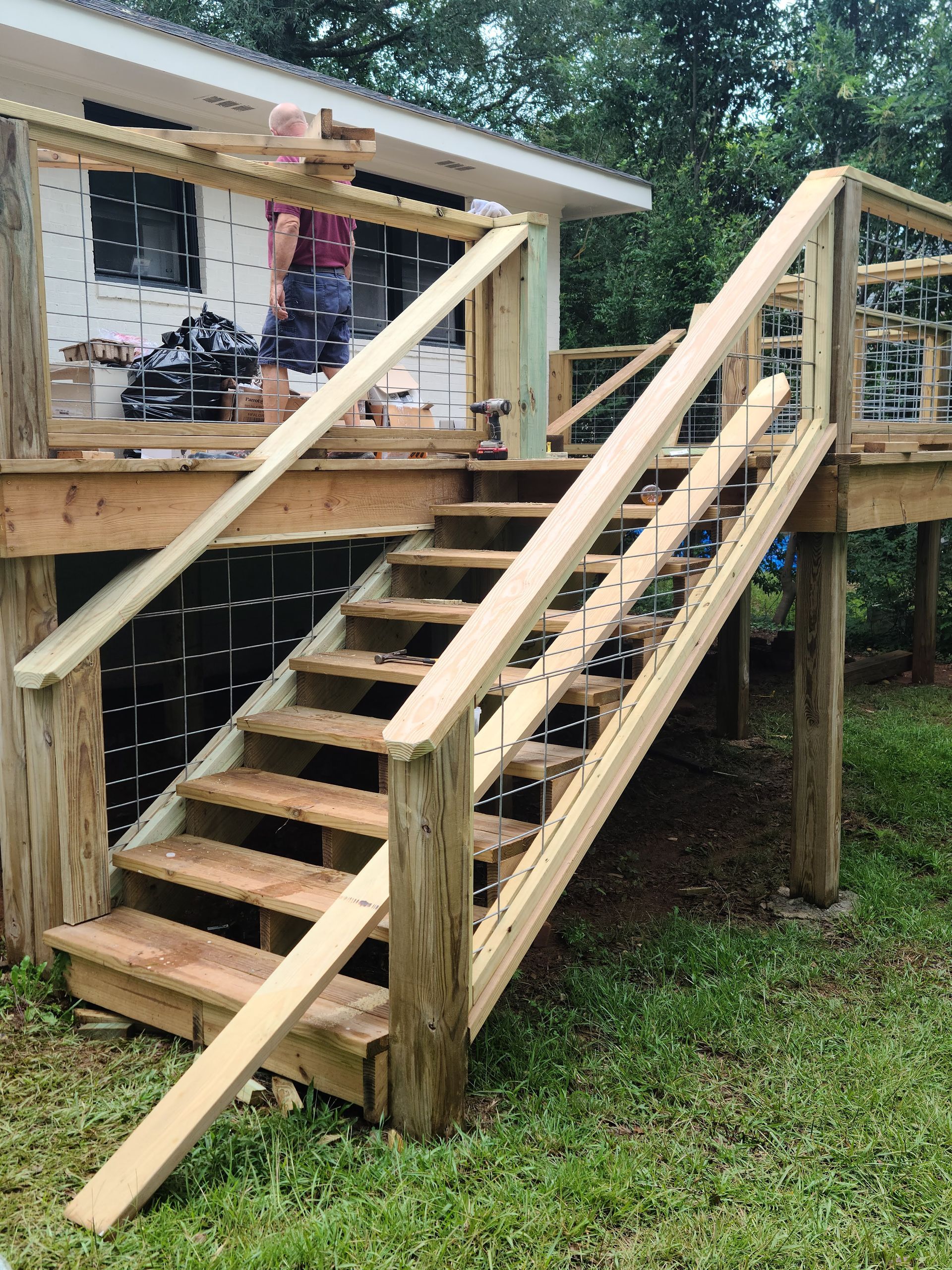 Wooden deck and staircase construction, unfinished with a person visible on the deck.