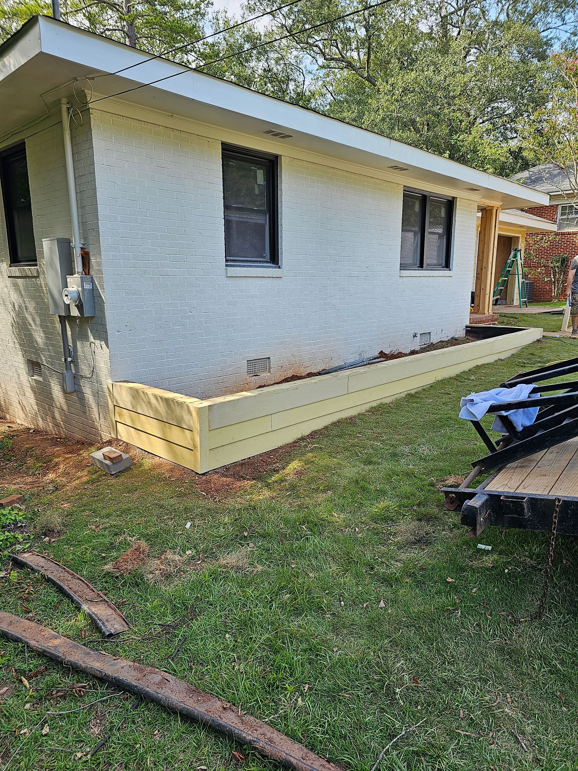 Exterior of a light-colored house with black windows, with a new yellow planter box and grassy yard.