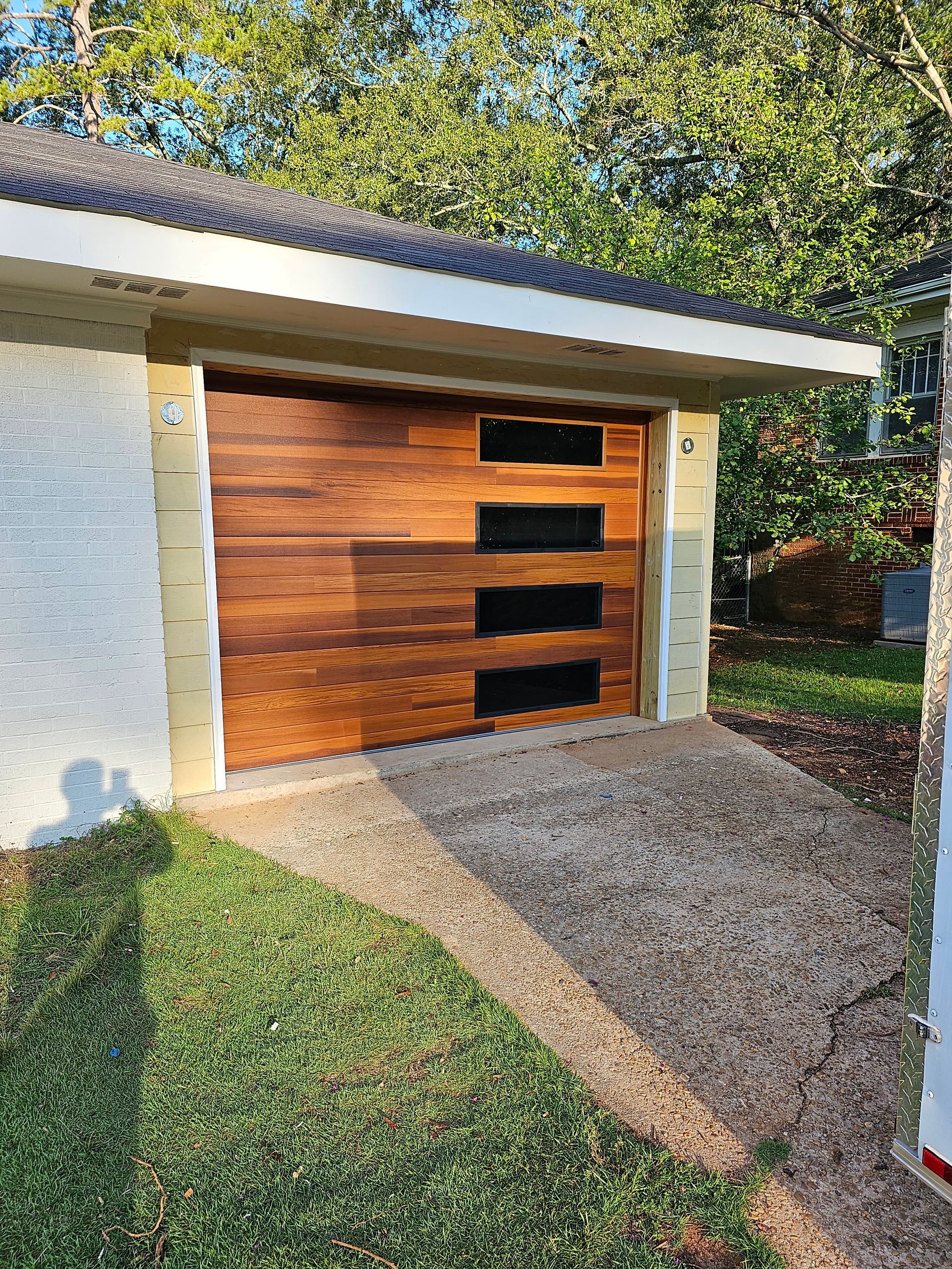 Wooden garage door with dark glass windows, set in a stucco building, with concrete ramp and green grass.