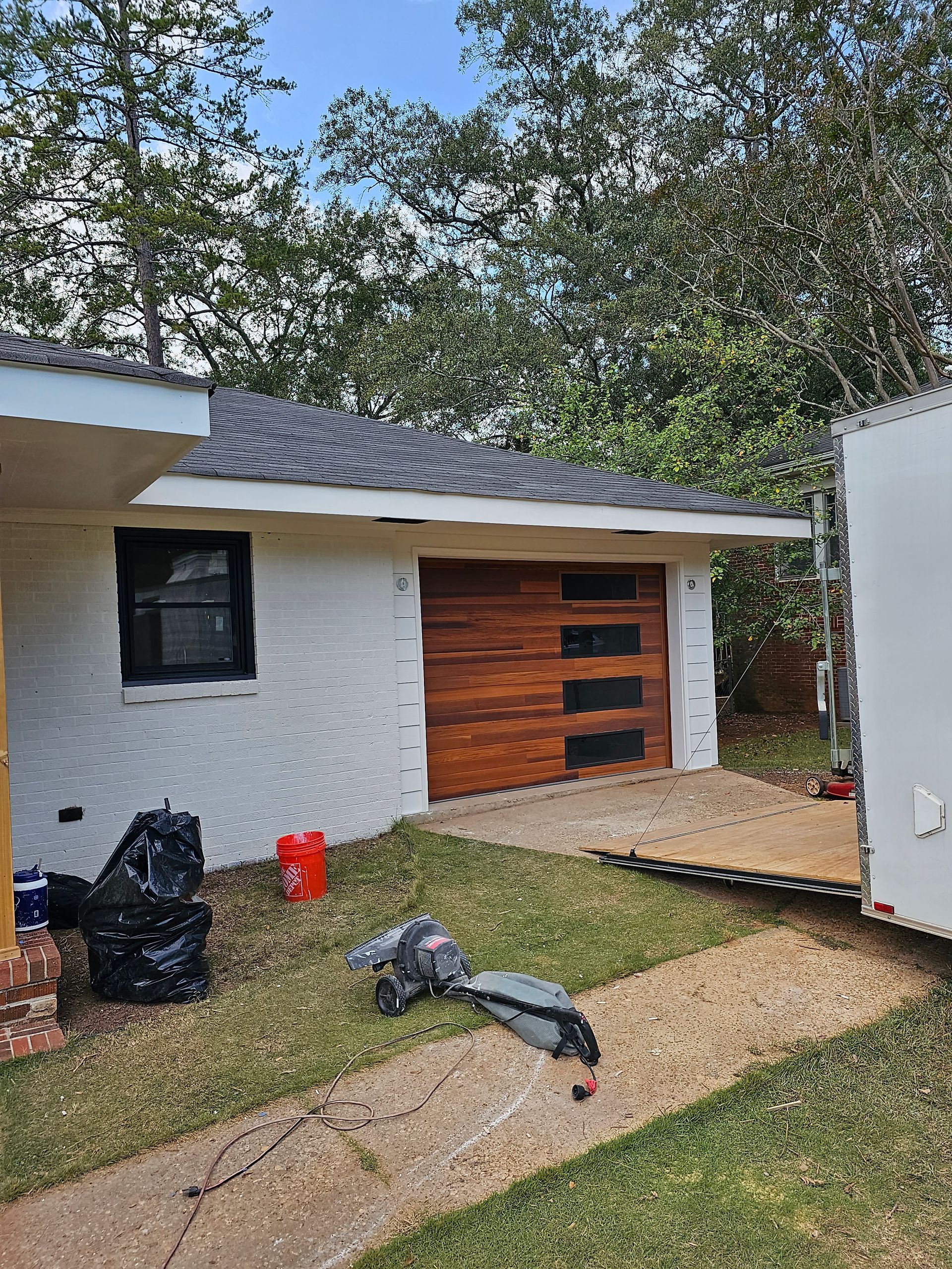 White brick building with a brown garage door. A black window and trash bags sit nearby.