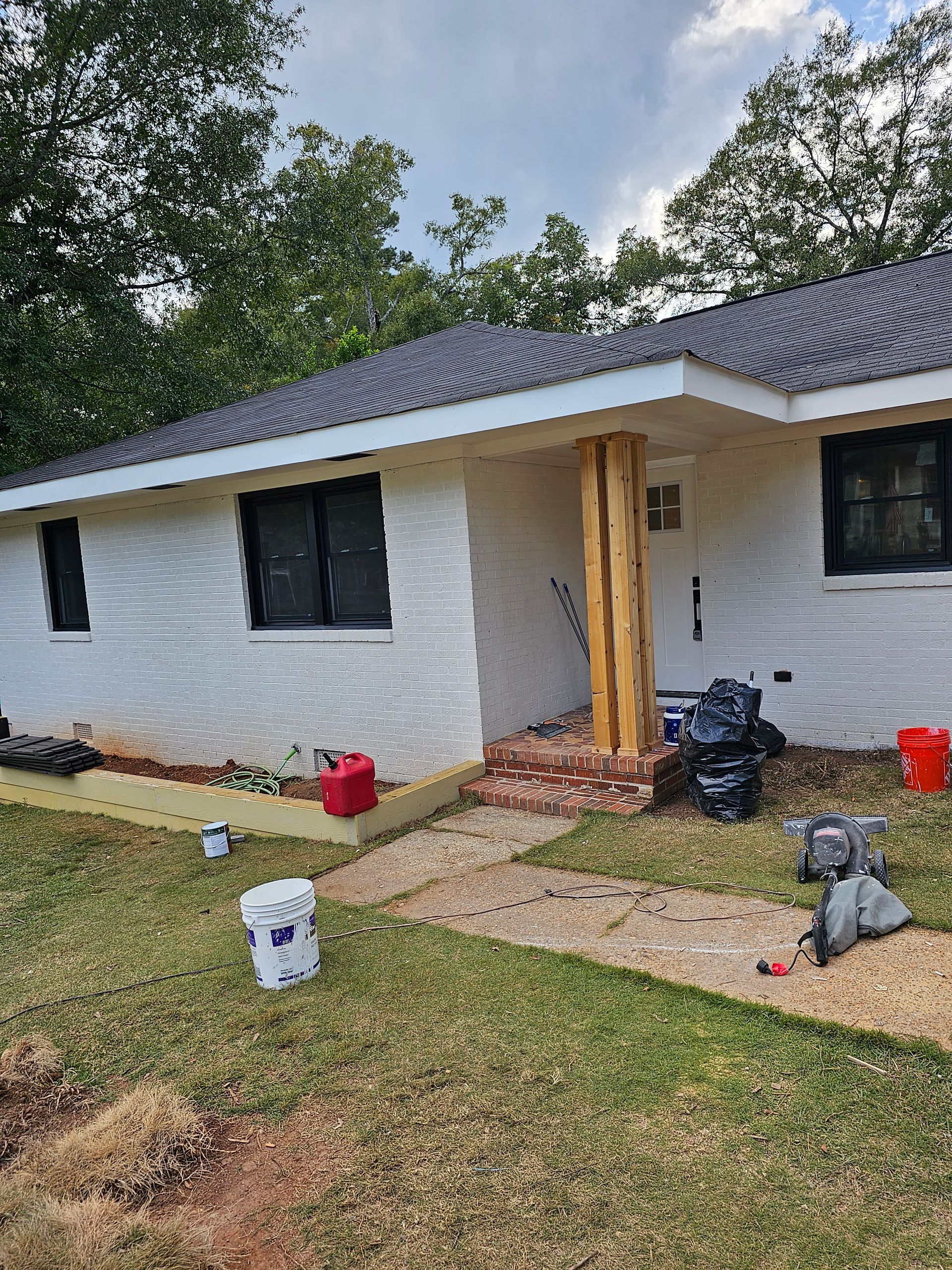 White painted brick house with wooden columns on a small porch; supplies and trash bags on the ground.