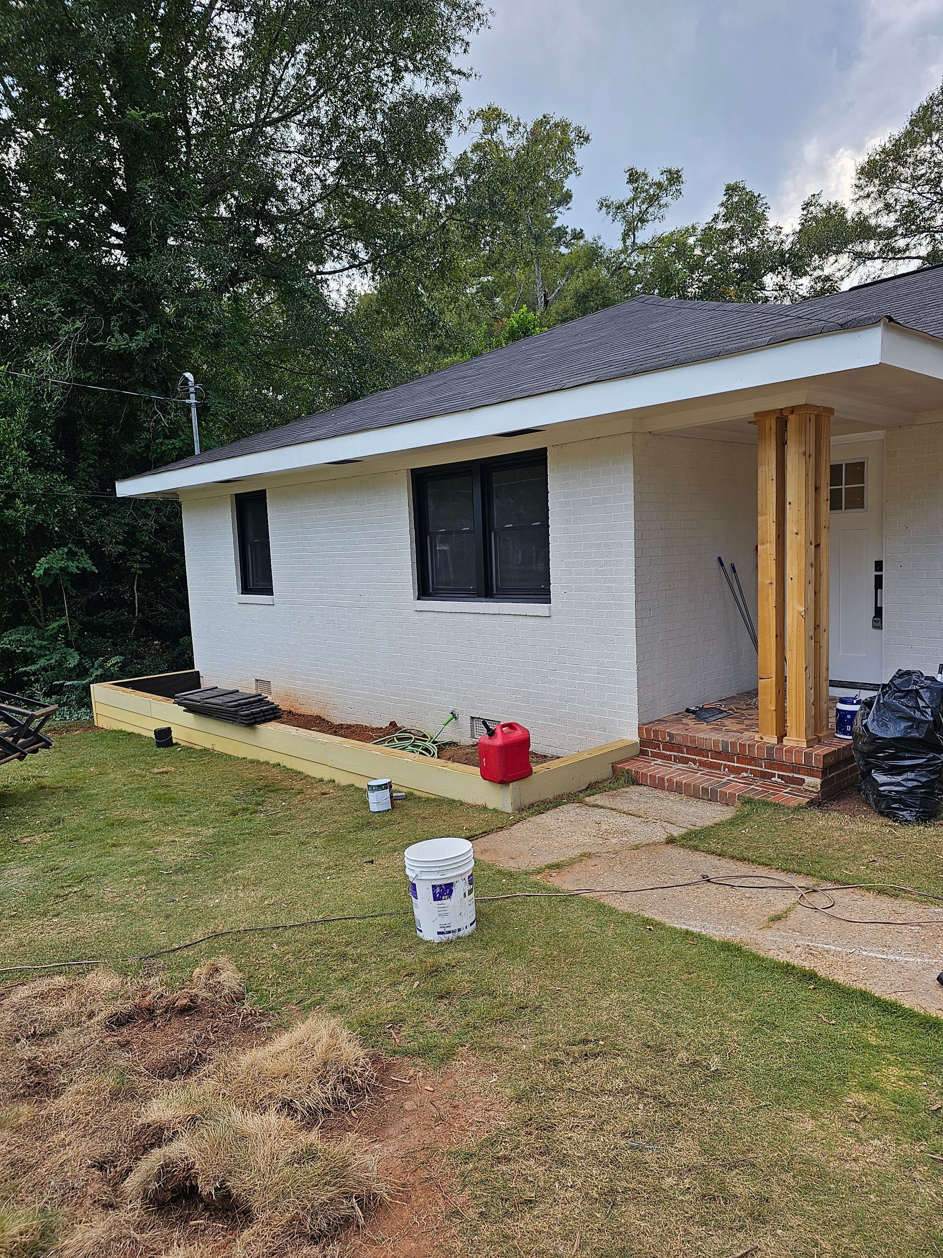 White house with black windows and wooden beams. Red brick porch, paint cans in the yard.
