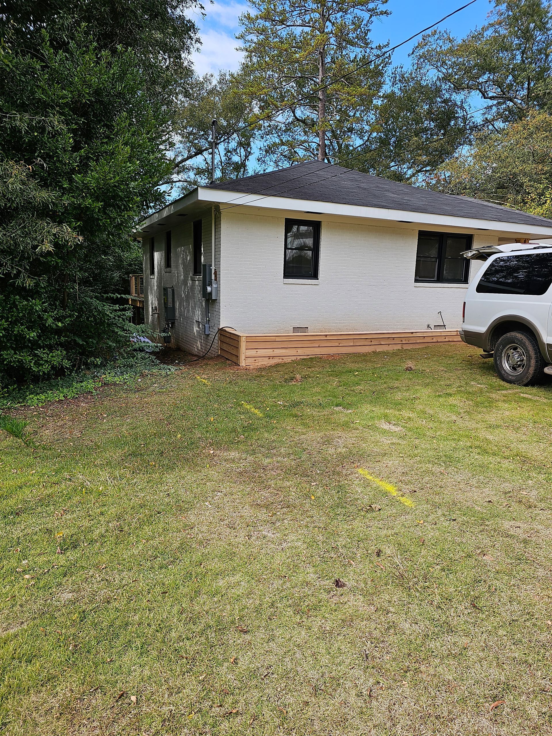 A small, white-painted brick house with a dark roof and a lawn; a white truck is parked nearby.