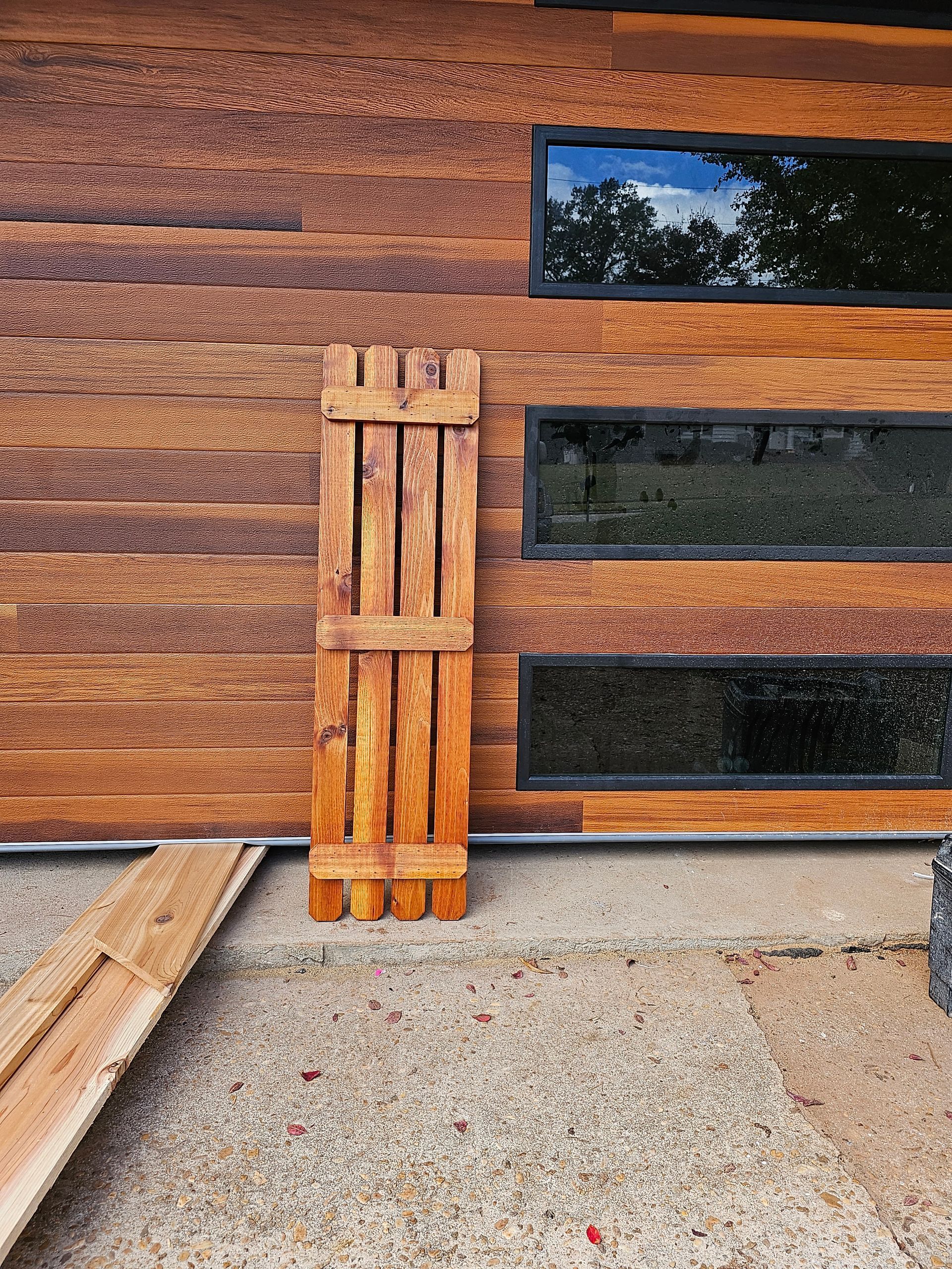 Wooden shutter propped against a wood-paneled wall with three horizontal windows.