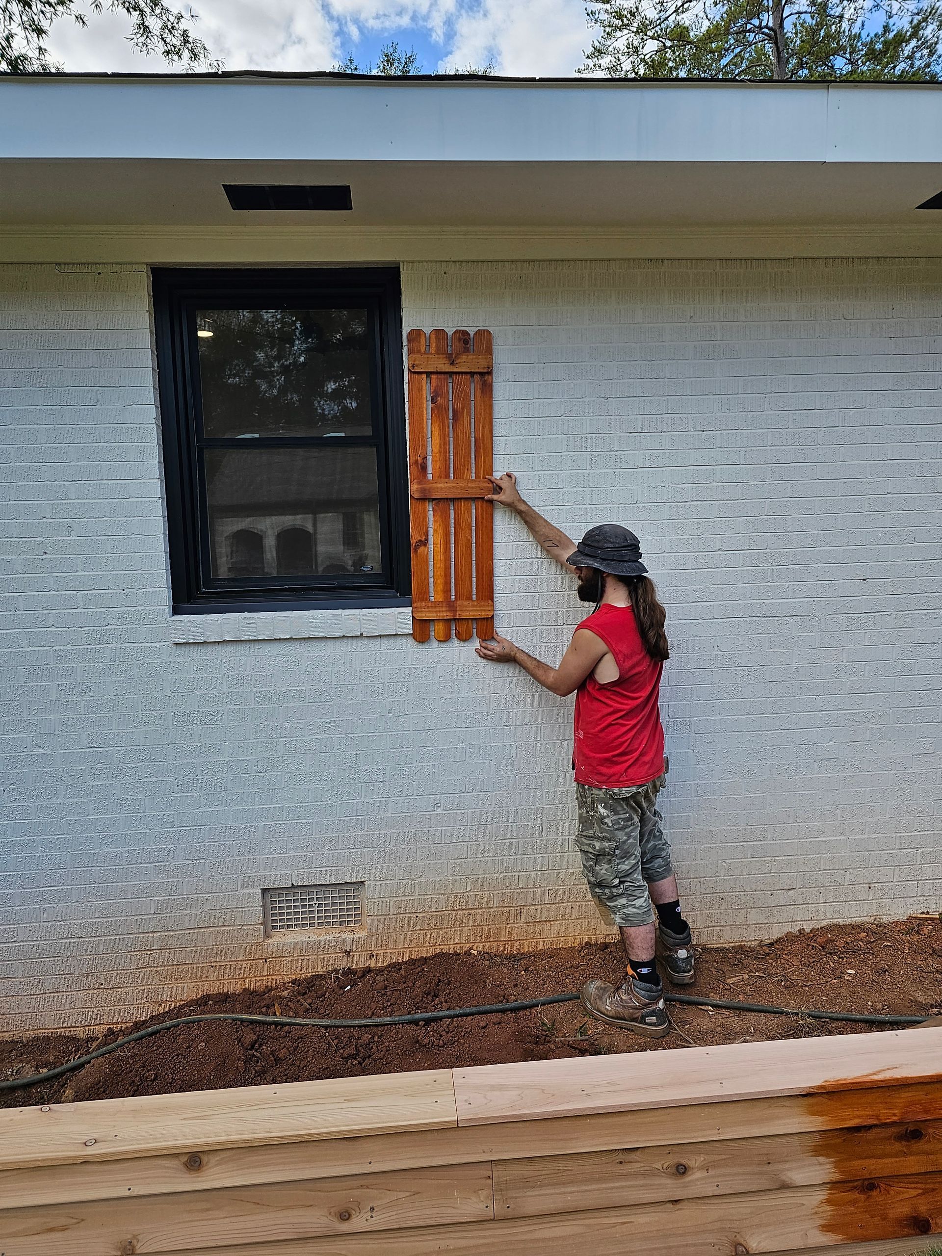 Person installing a wooden shutter on a brick wall next to a window.