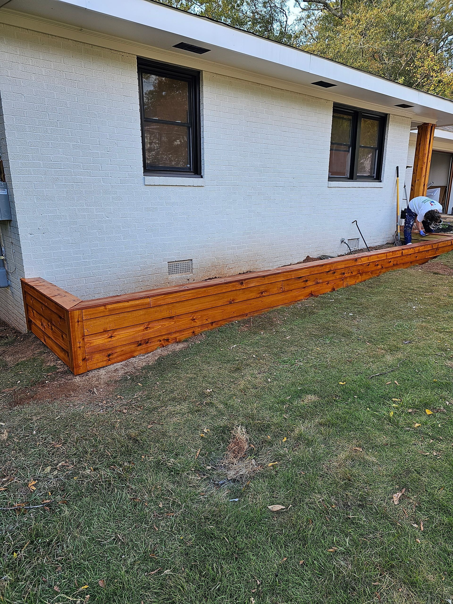 A newly built, stained wood planter box runs along the side of a white stucco building.
