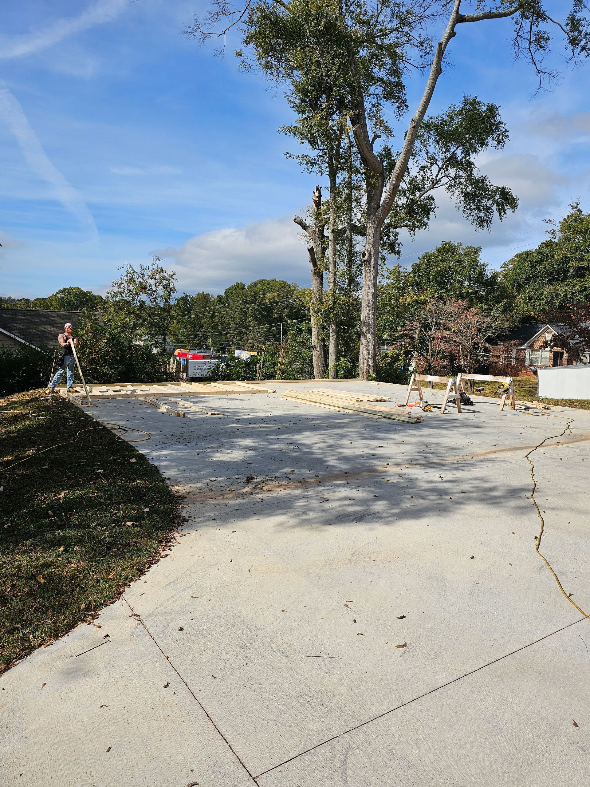 Concrete driveway with a tree being trimmed under a blue sky. Person on the left.