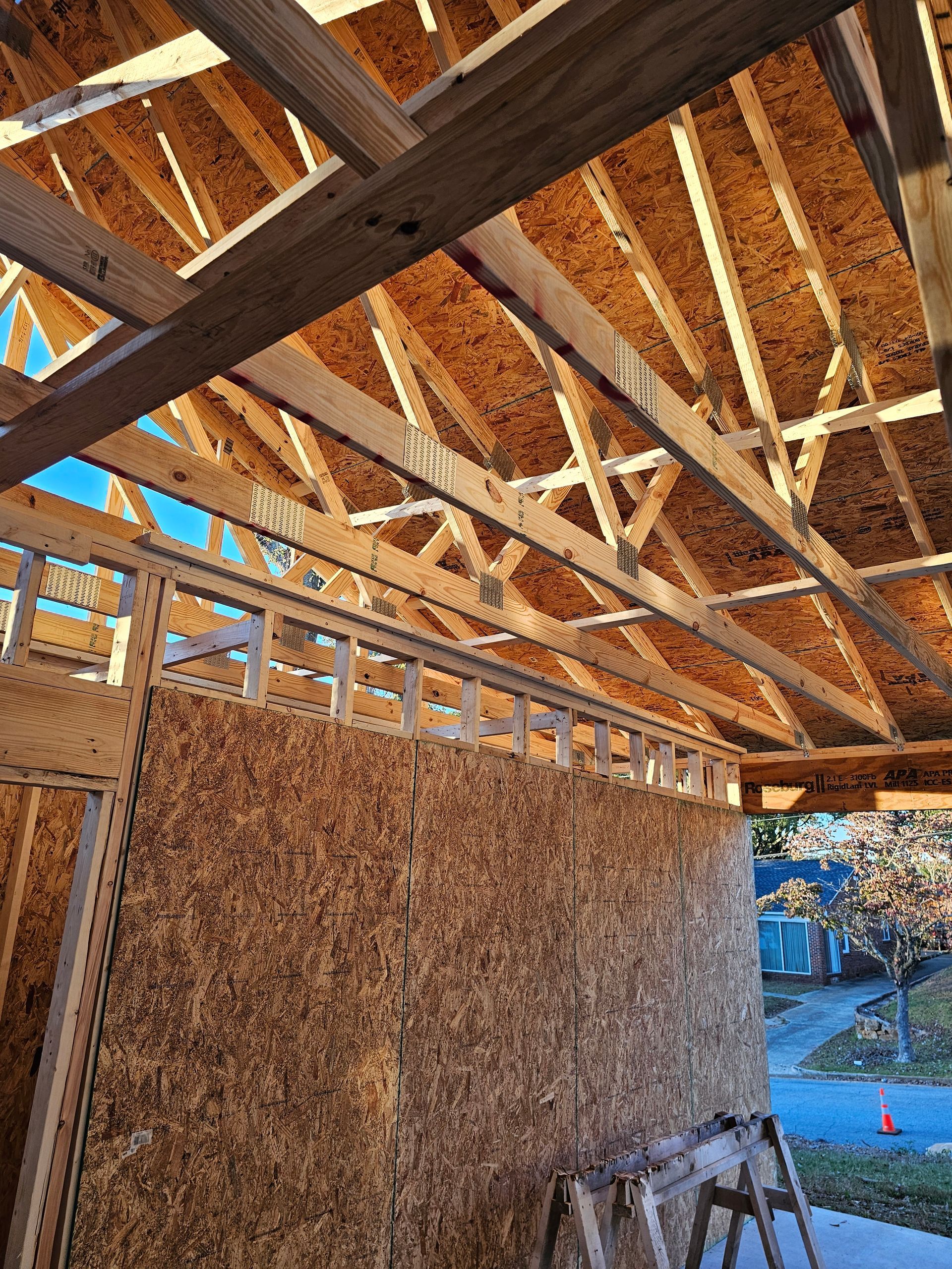 Wooden framework of a building's roof under construction; OSB sheathing on the walls; sky visible.