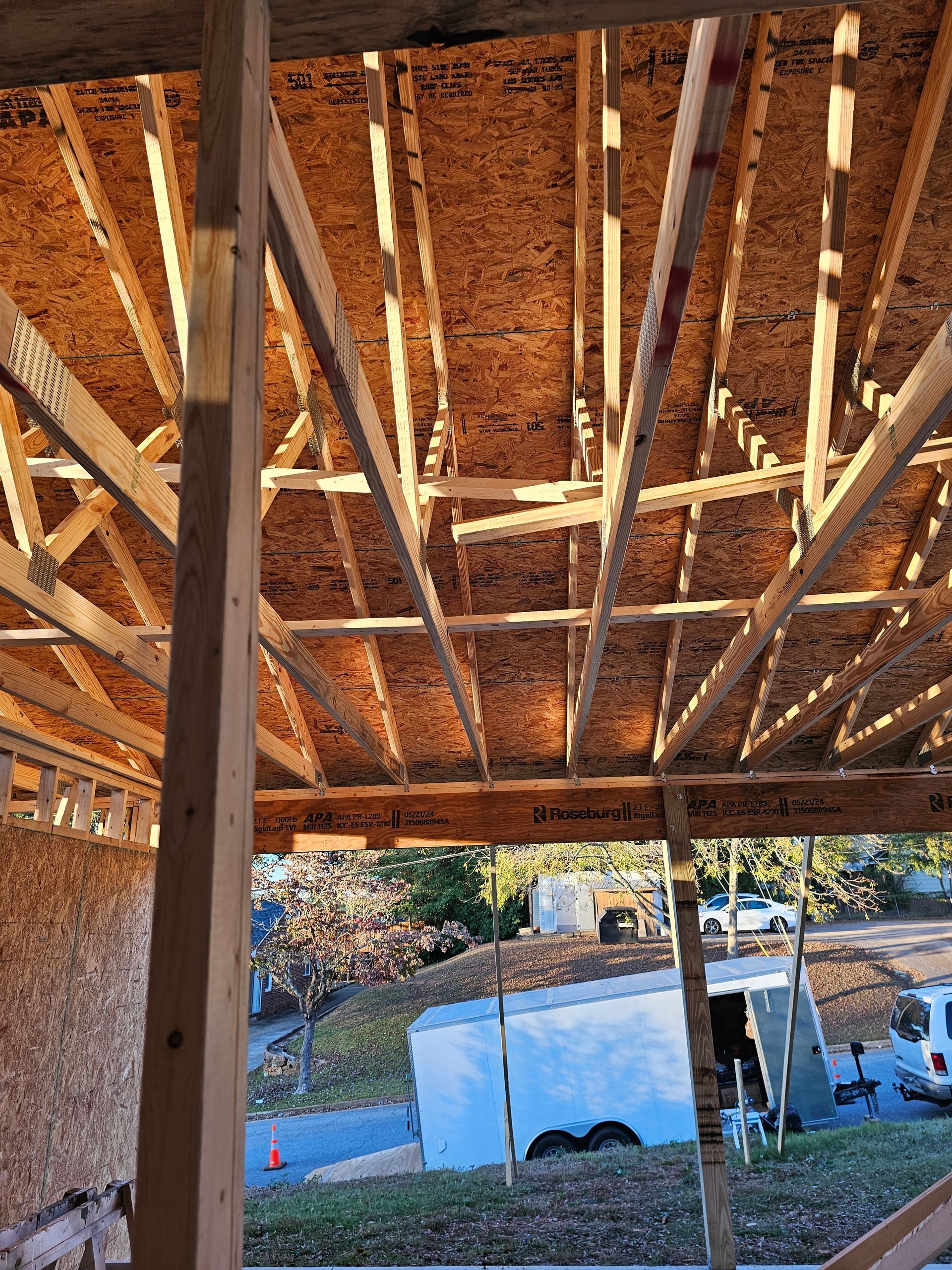 Construction framing with exposed wood rafters, looking out at a street scene with trailers.