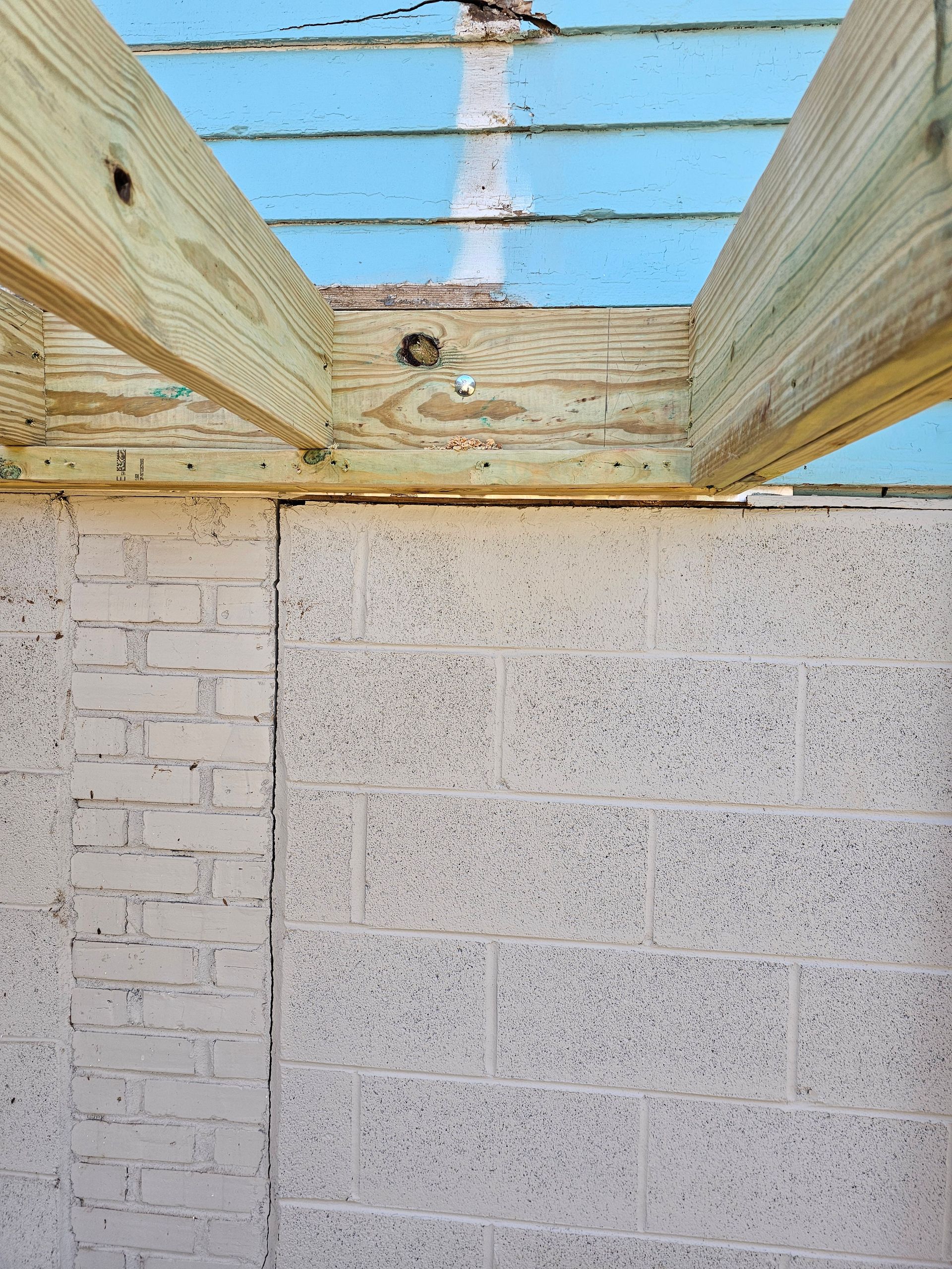 Wooden beams over a block wall. Blue siding is visible above the beams.
