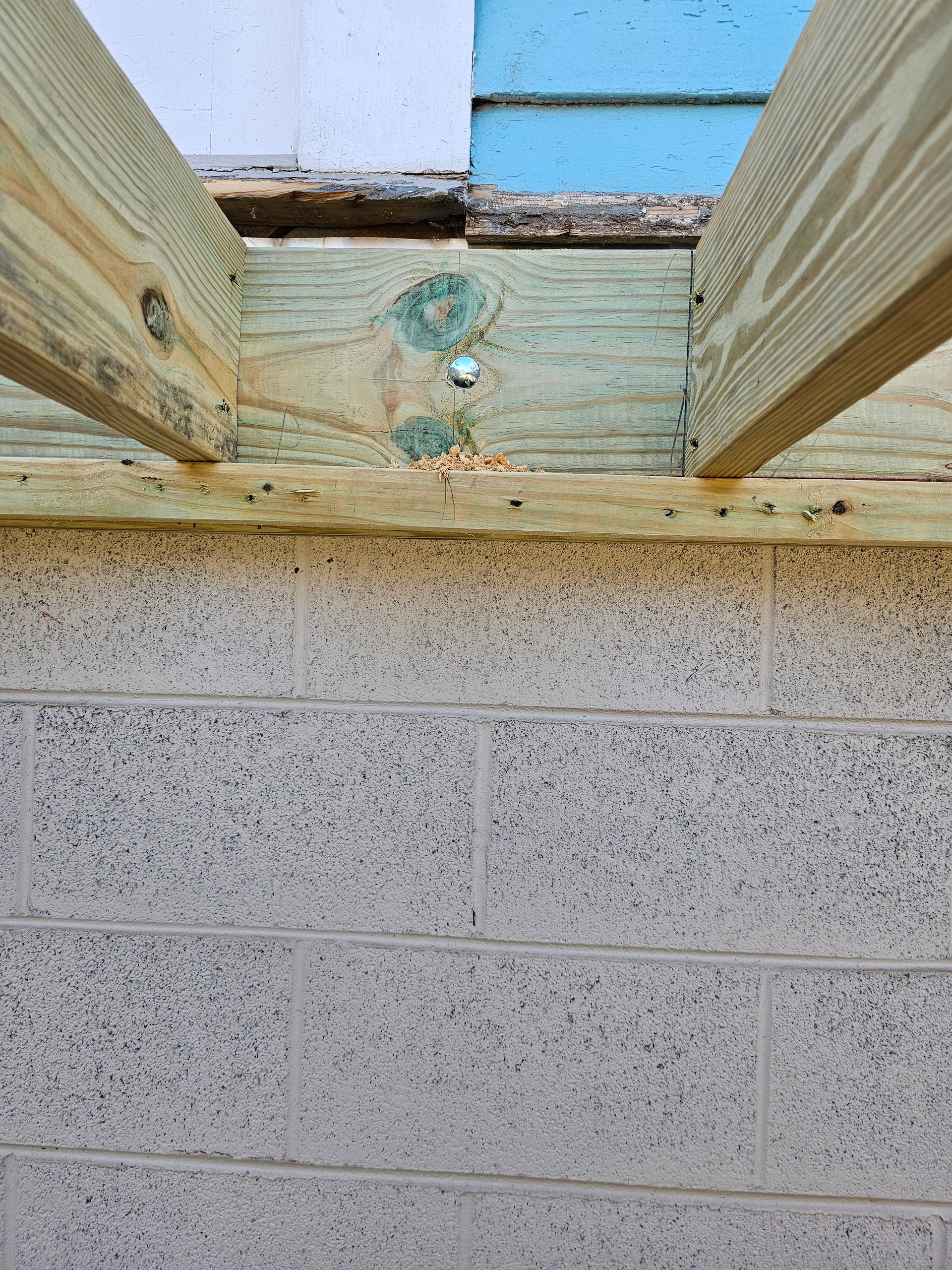 Wooden beams connected to a concrete block wall, with a layer of blue and white insulation above.
