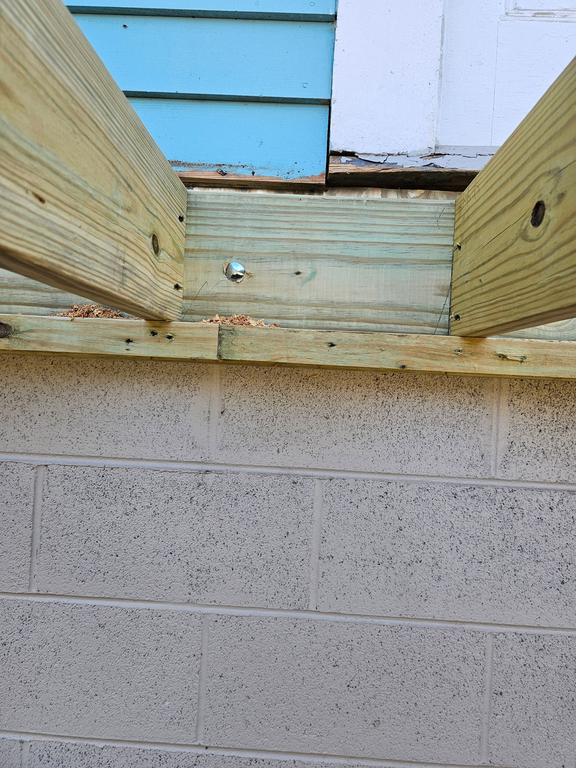 Wooden beams extending from a light blue wall, resting on a gray concrete block foundation.