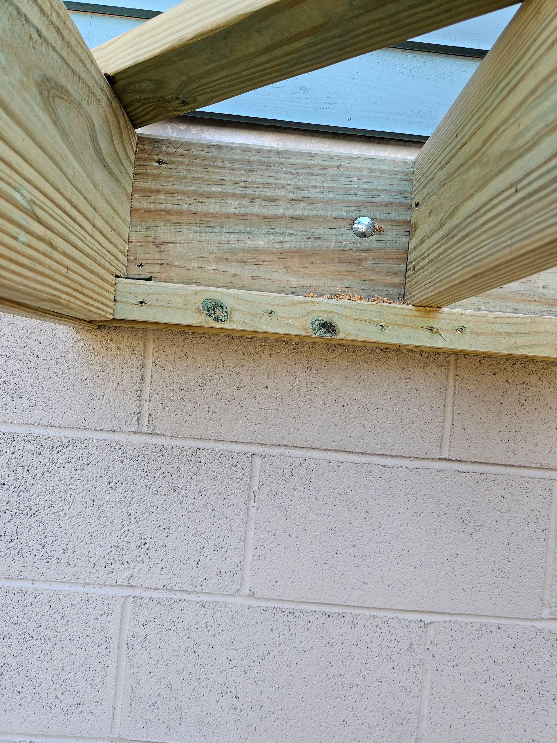 Wooden beams bolted to a concrete block wall, part of an outdoor structure.