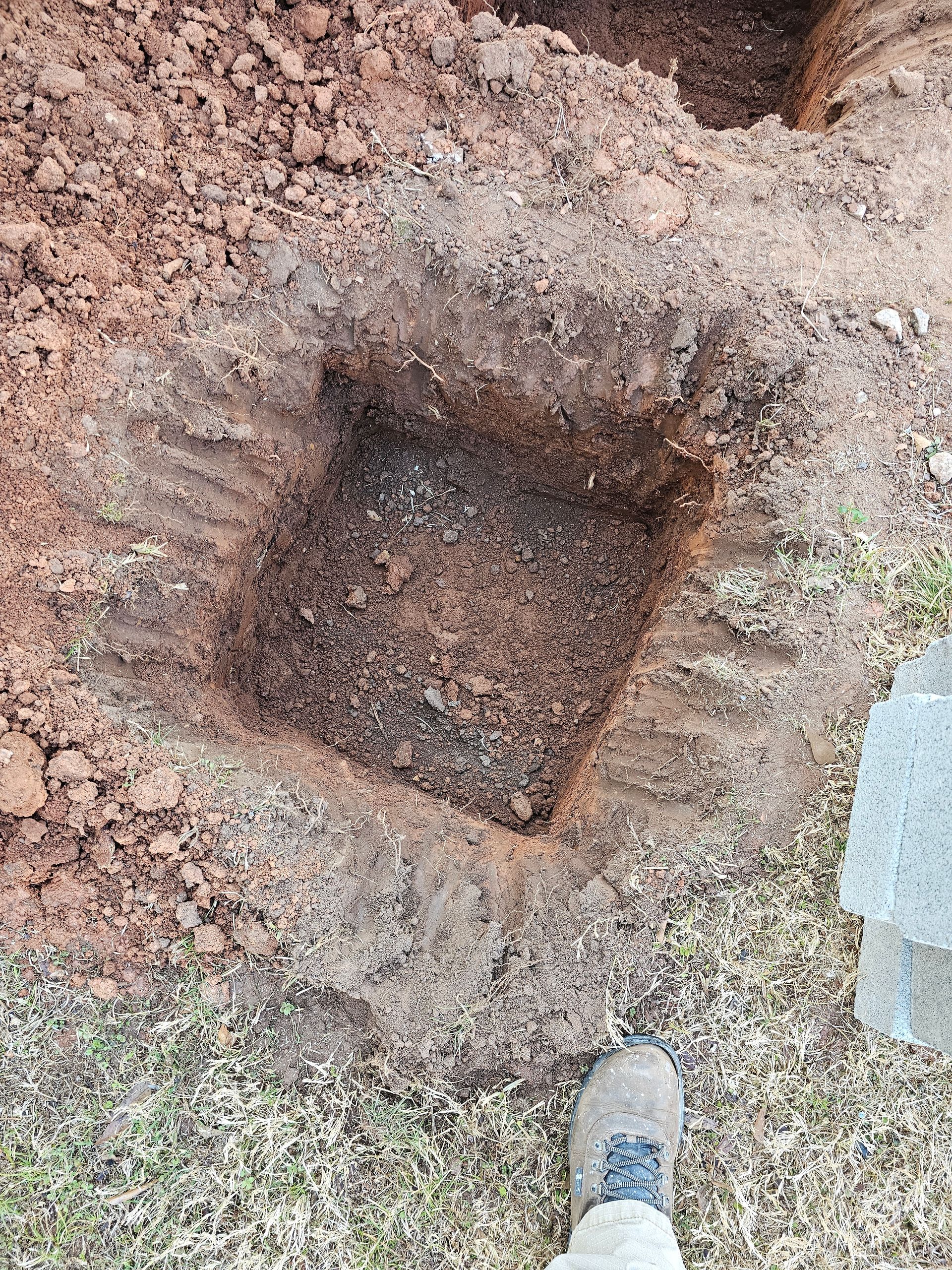 Square hole dug in dirt, foot visible at bottom right.
