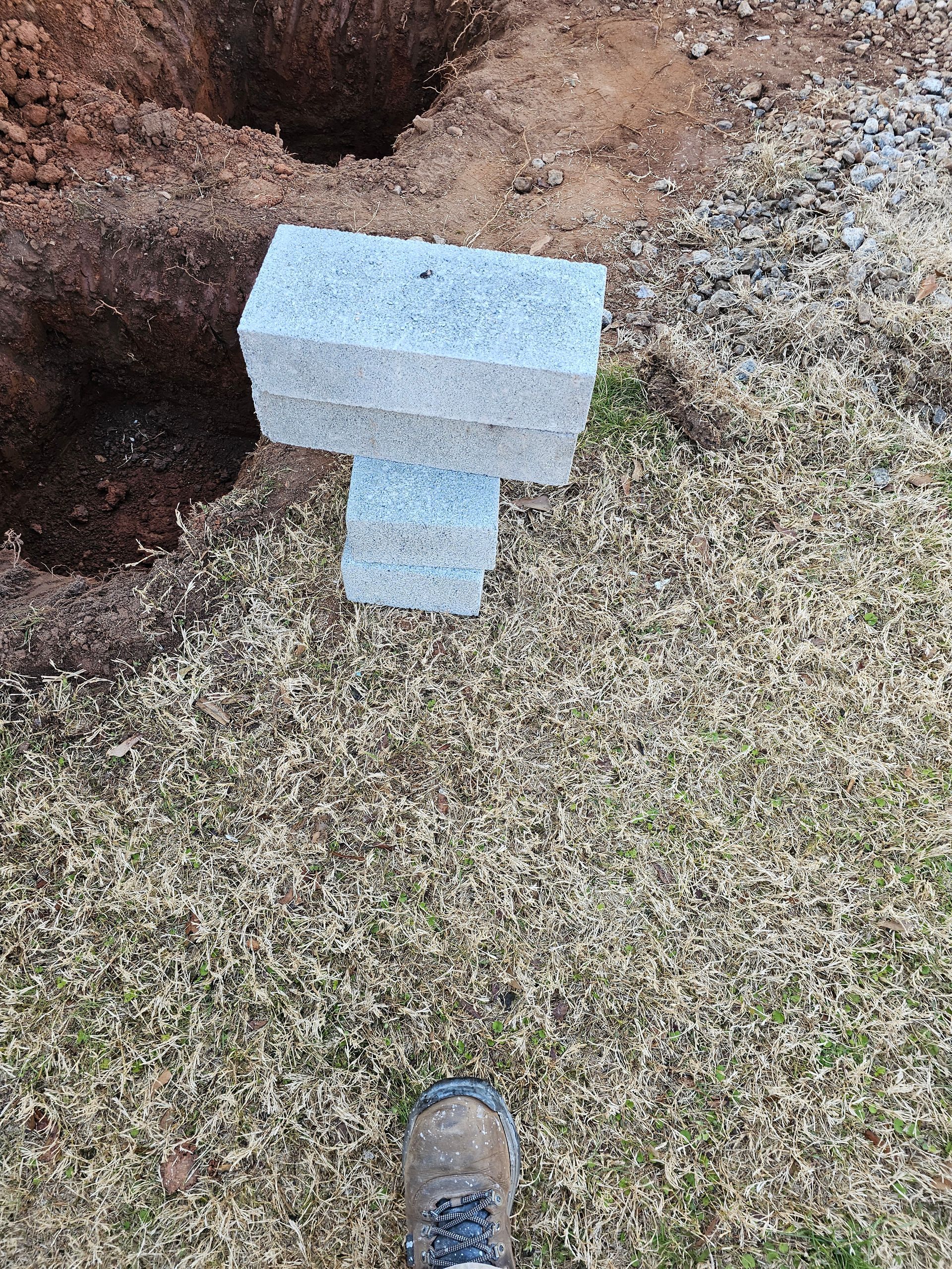 Gray cinder blocks stacked near a hole in the dirt, next to brown grass.