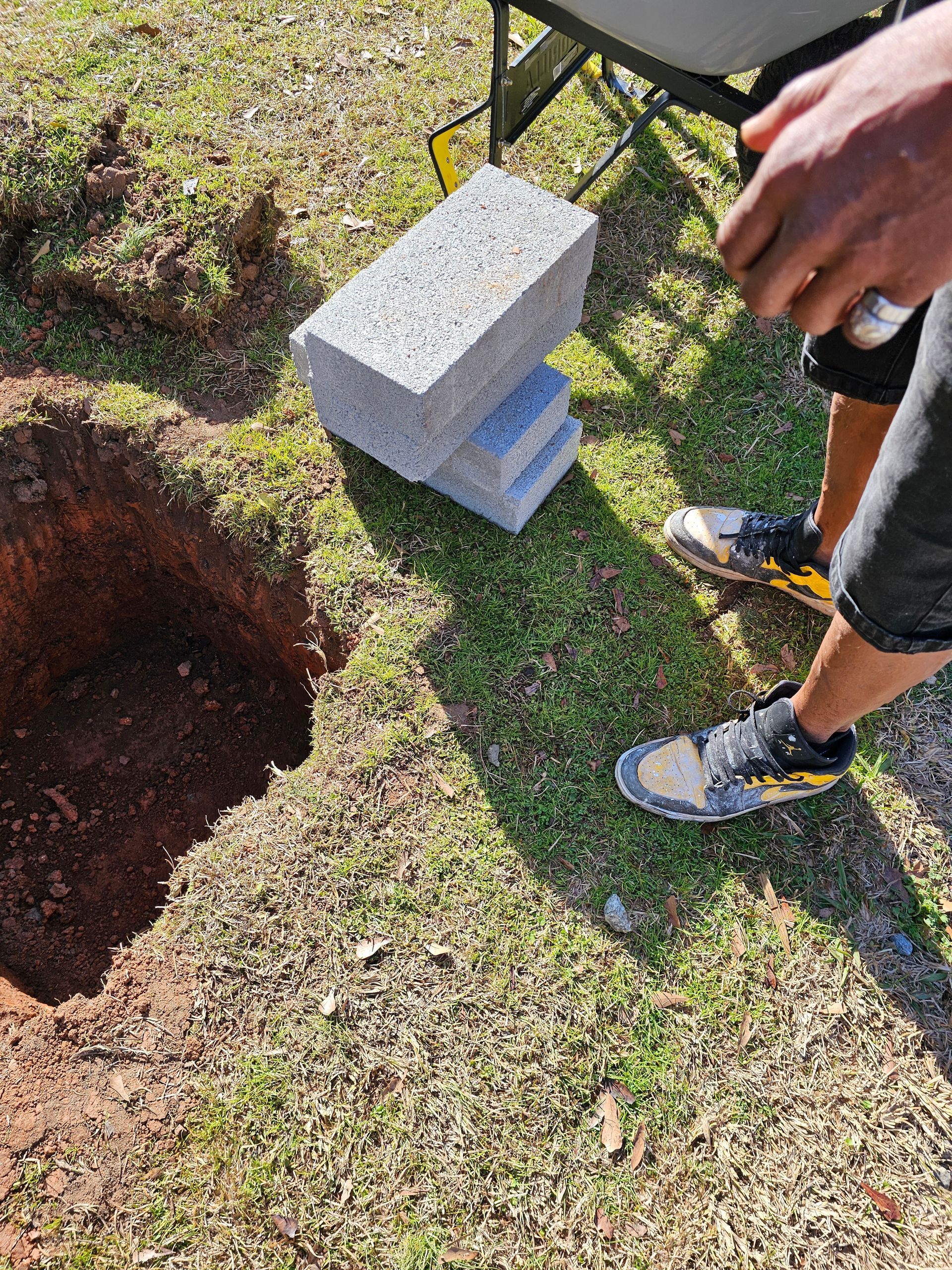 Hole in the ground next to concrete blocks and a person wearing sneakers.