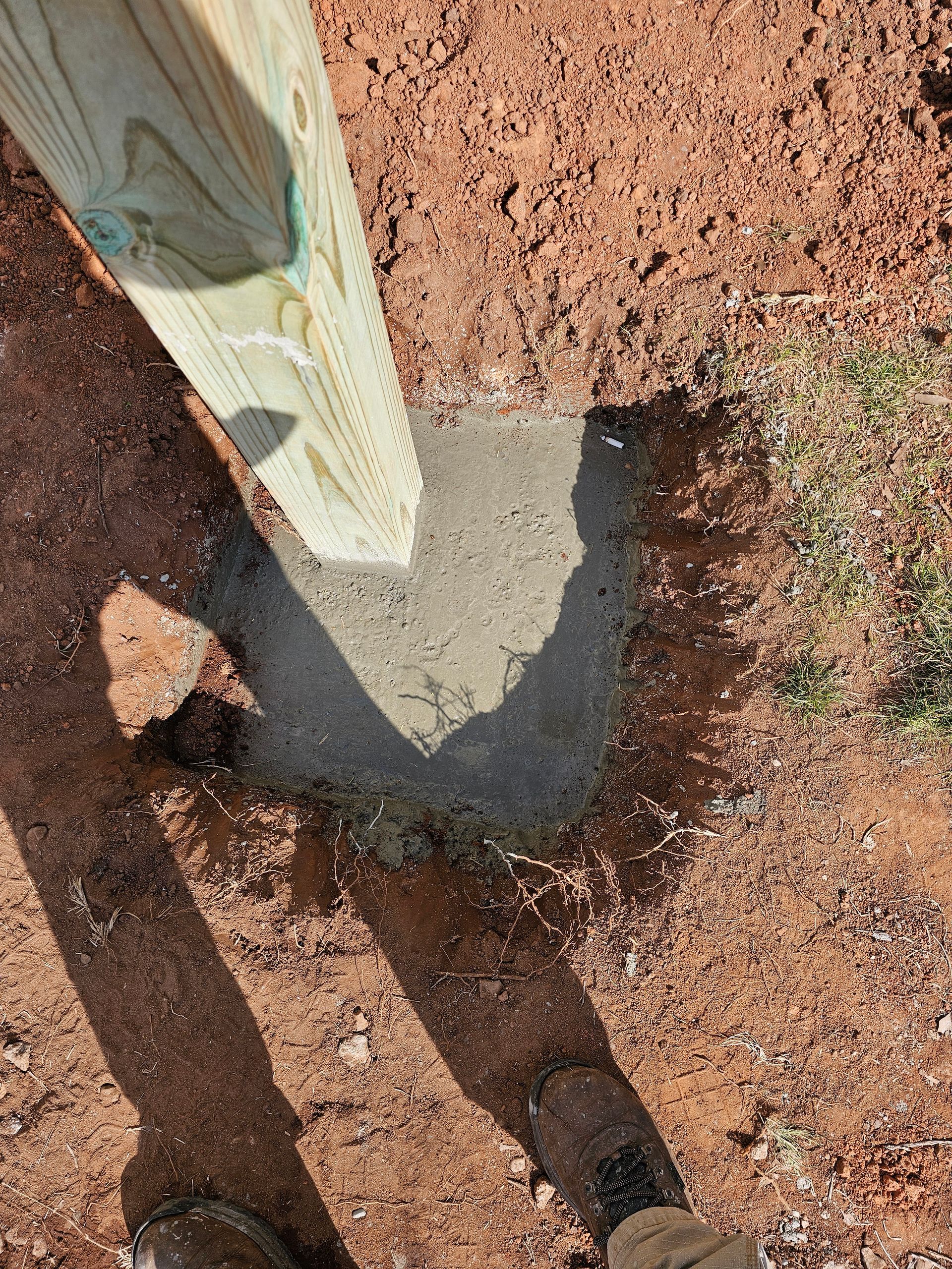 Wooden post set in concrete base on red dirt.