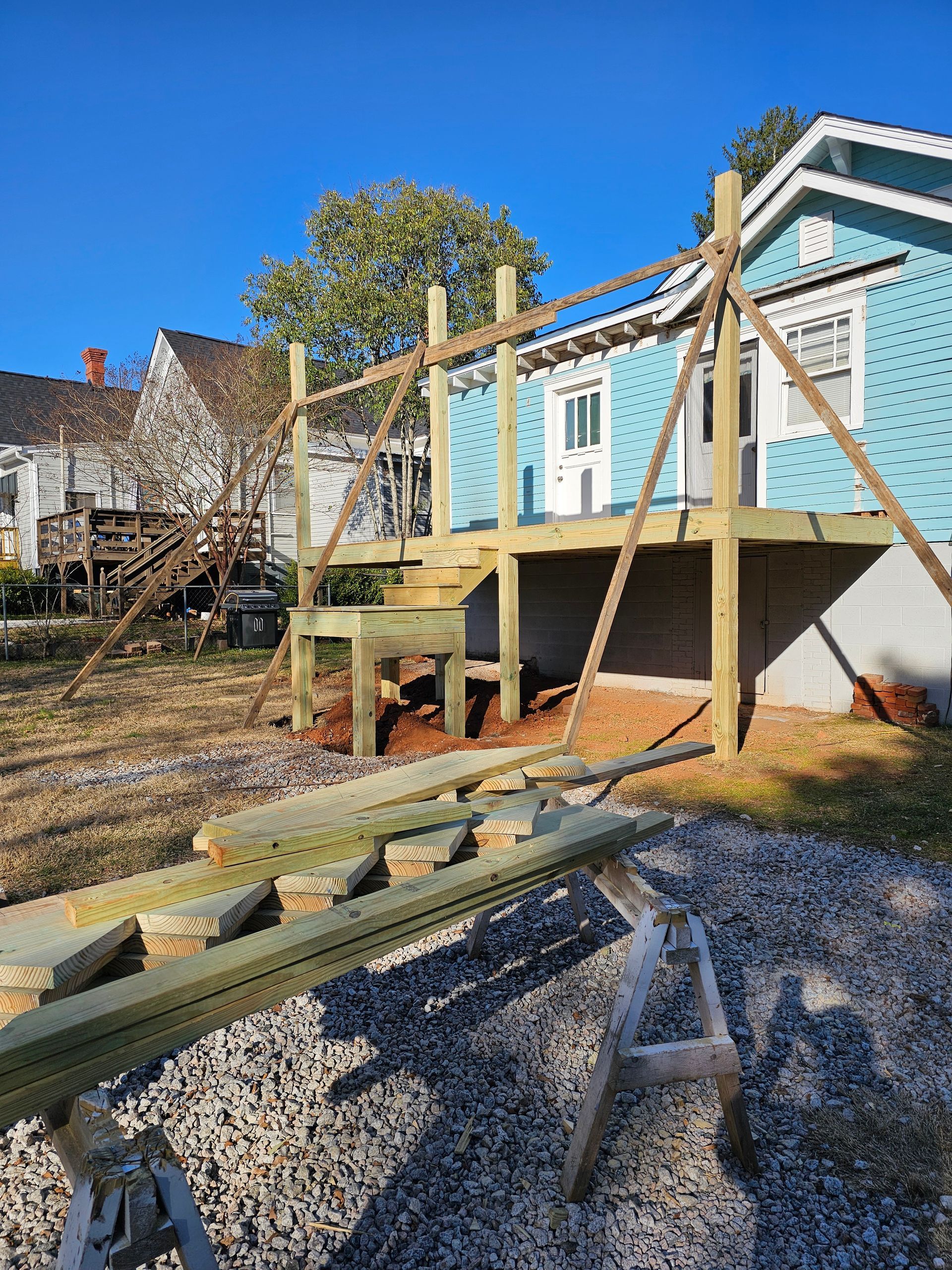 A wooden deck under construction next to a blue house on a sunny day.