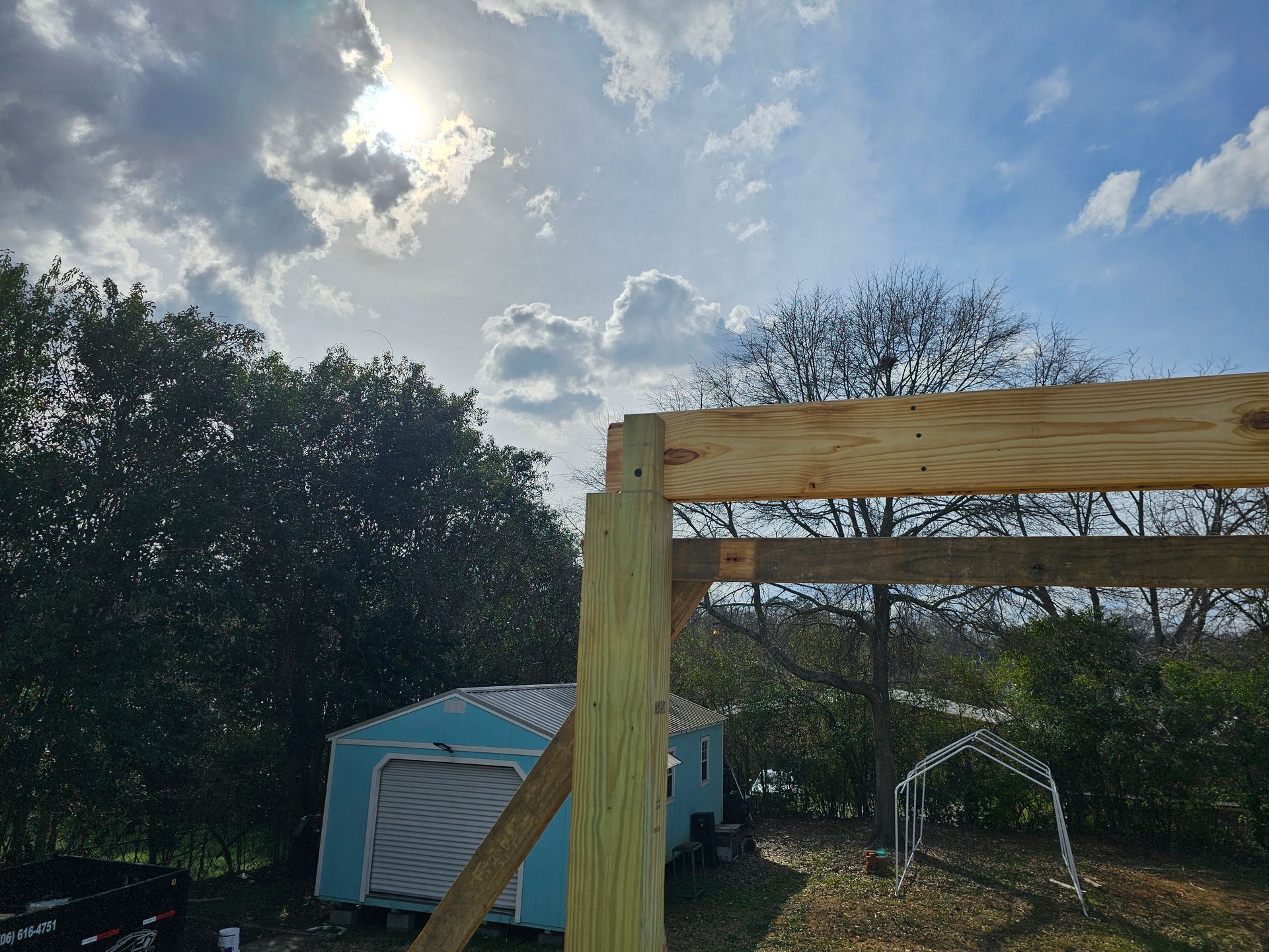 Wooden structure under construction against a cloudy sky with a small blue shed in the background.