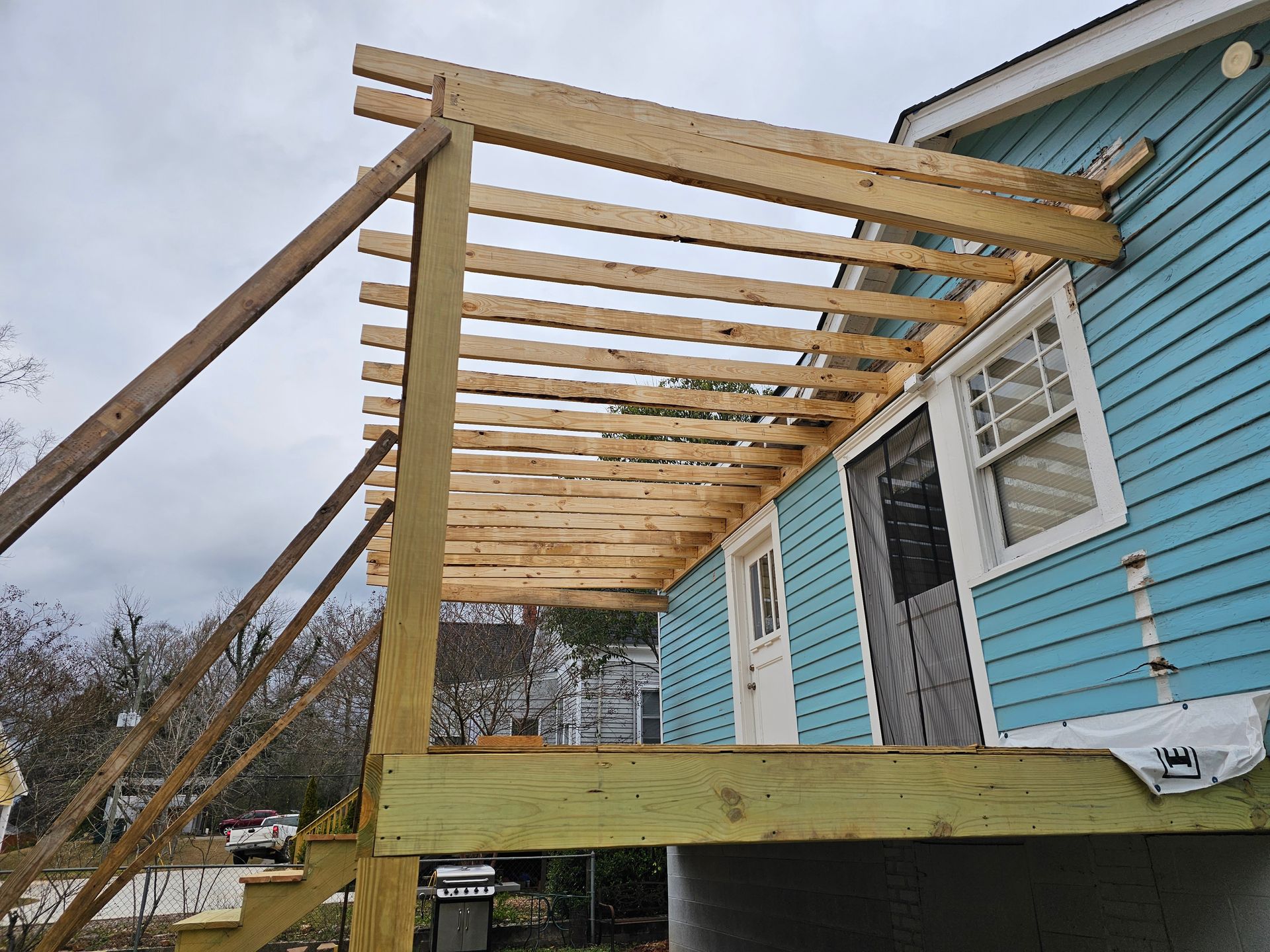 Deck construction in progress with wood framing attached to a light blue house.