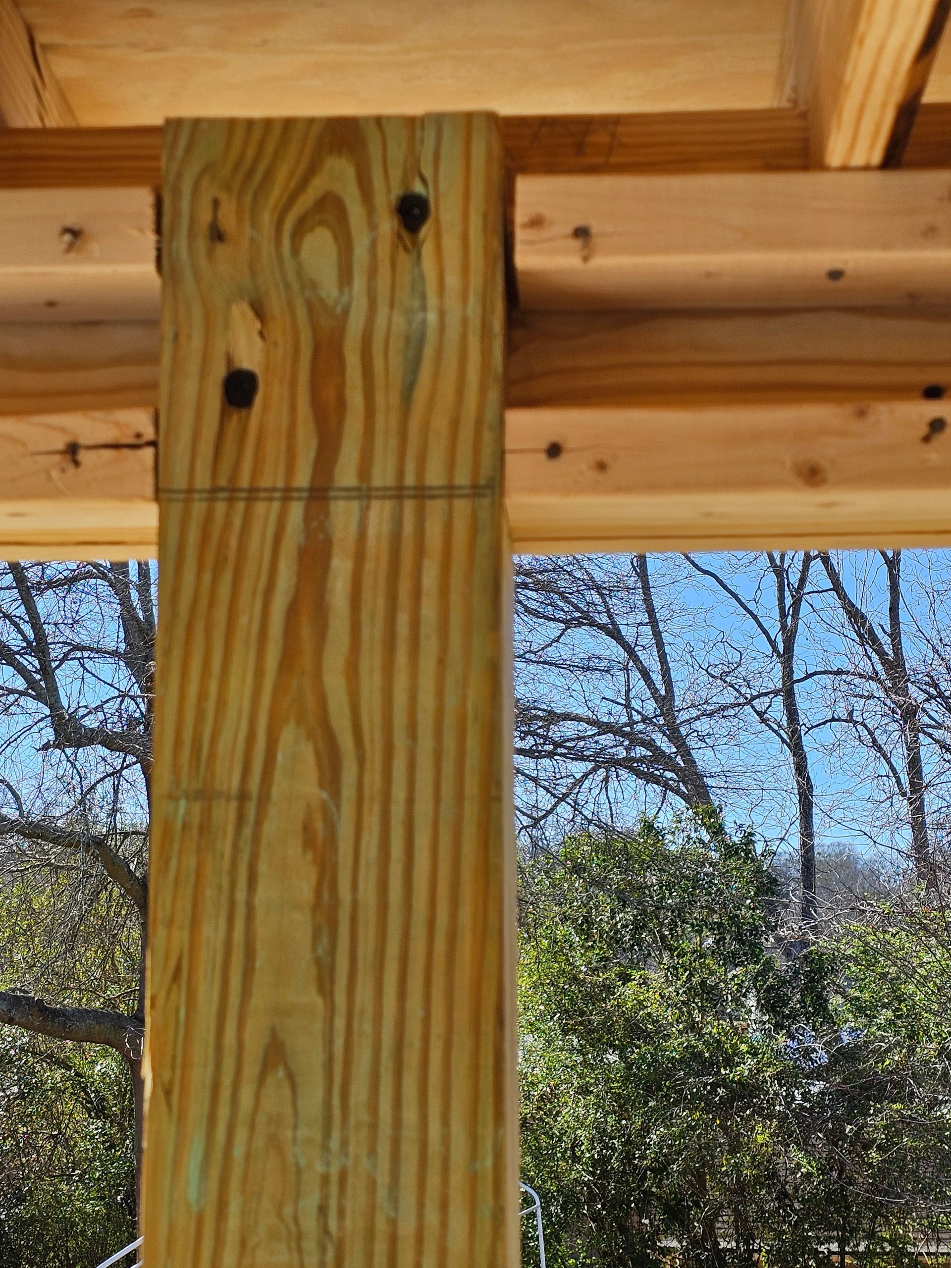 Wooden post attached to beams, view of trees and sky beyond.