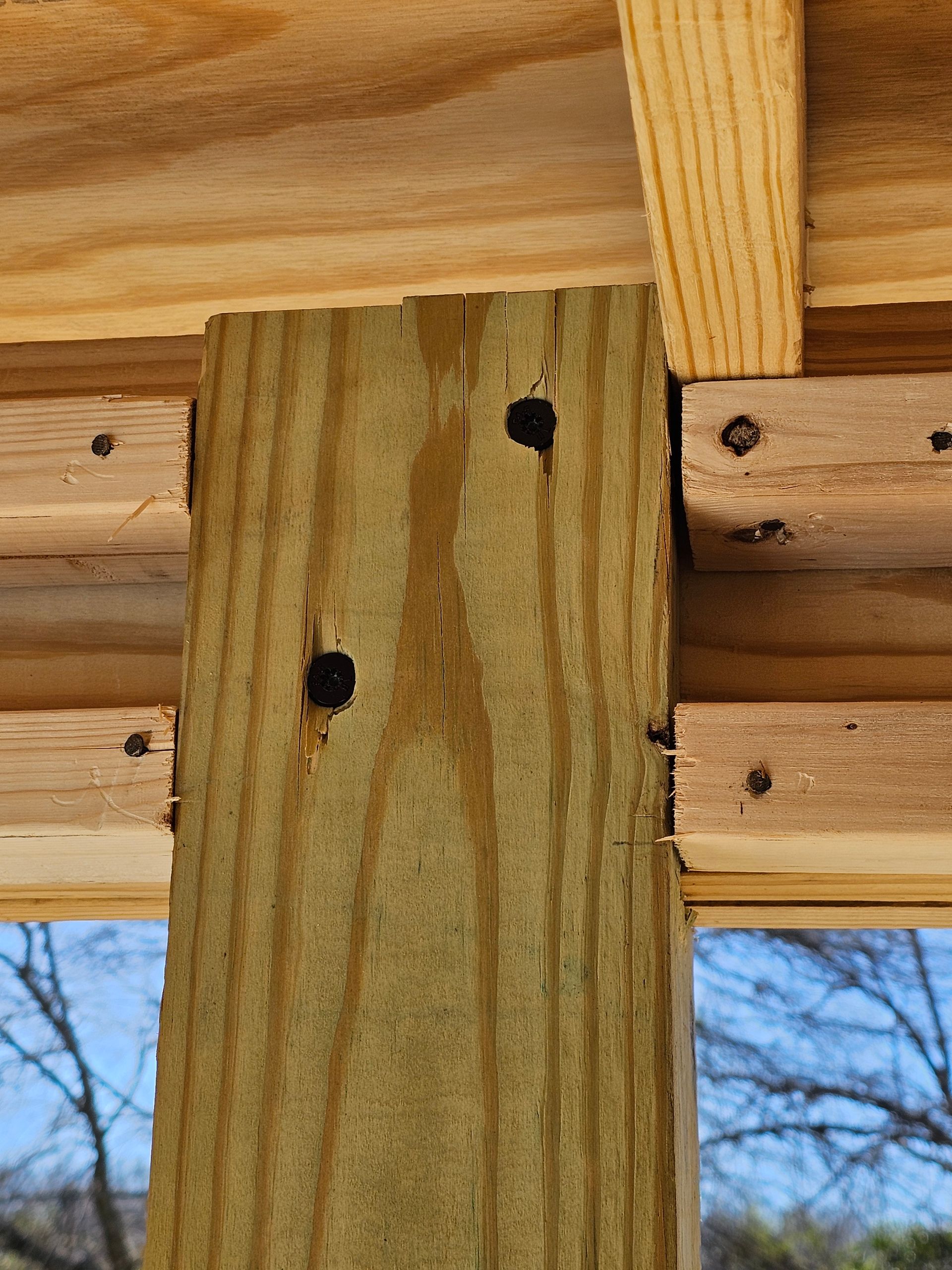 Wooden post joined to other wooden structures with nails. Outdoor setting, daylight.