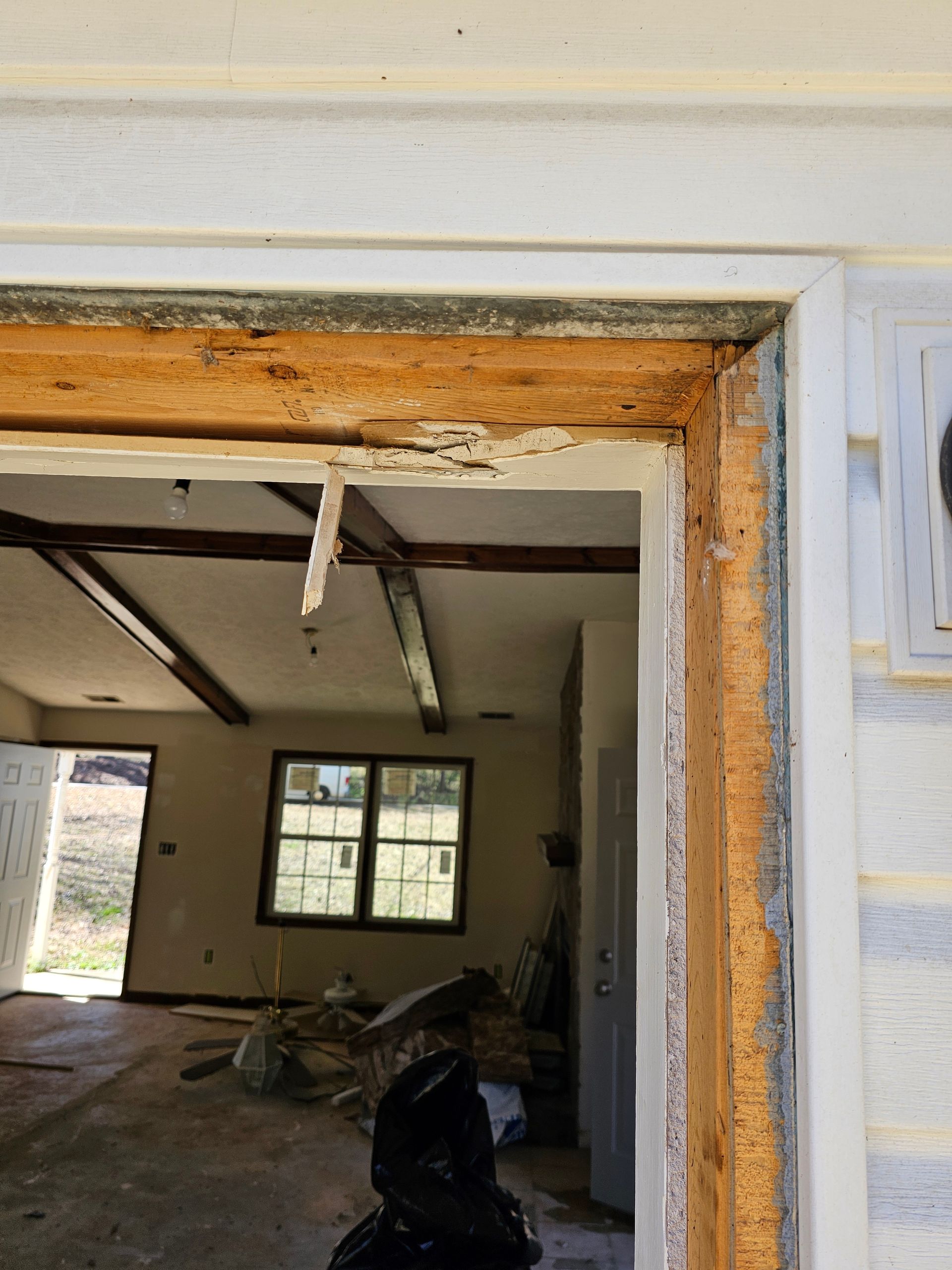 Exterior door frame with weathered wood and white trim, leading to a room with interior debris.