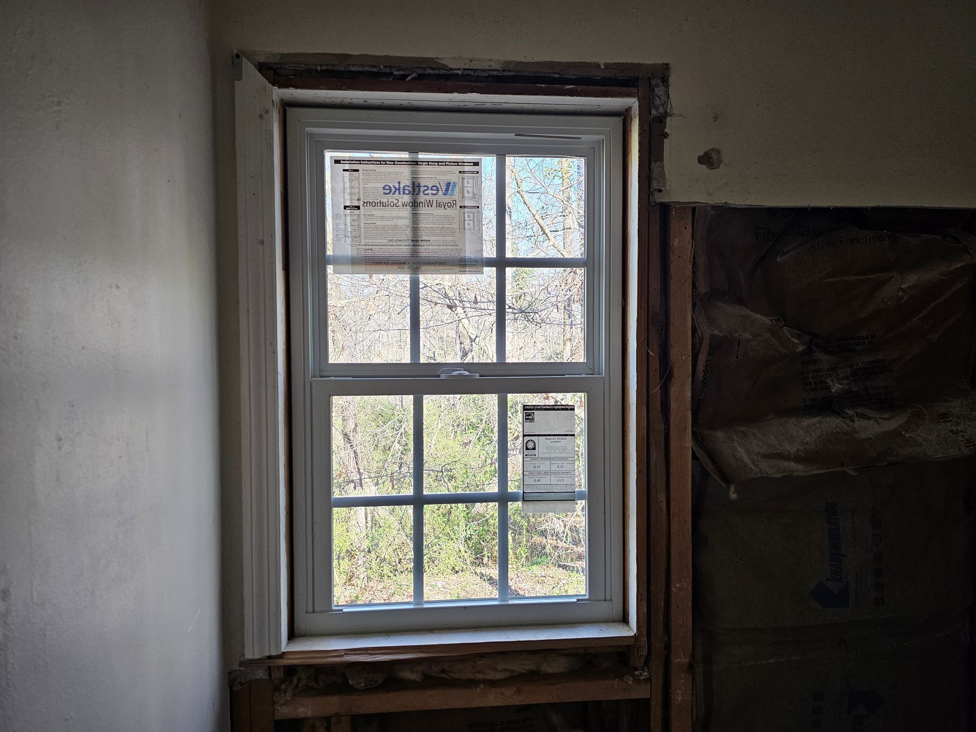 White double-hung window in a wall, framed with white trim. The surrounding wall is unfinished, with exposed studs.