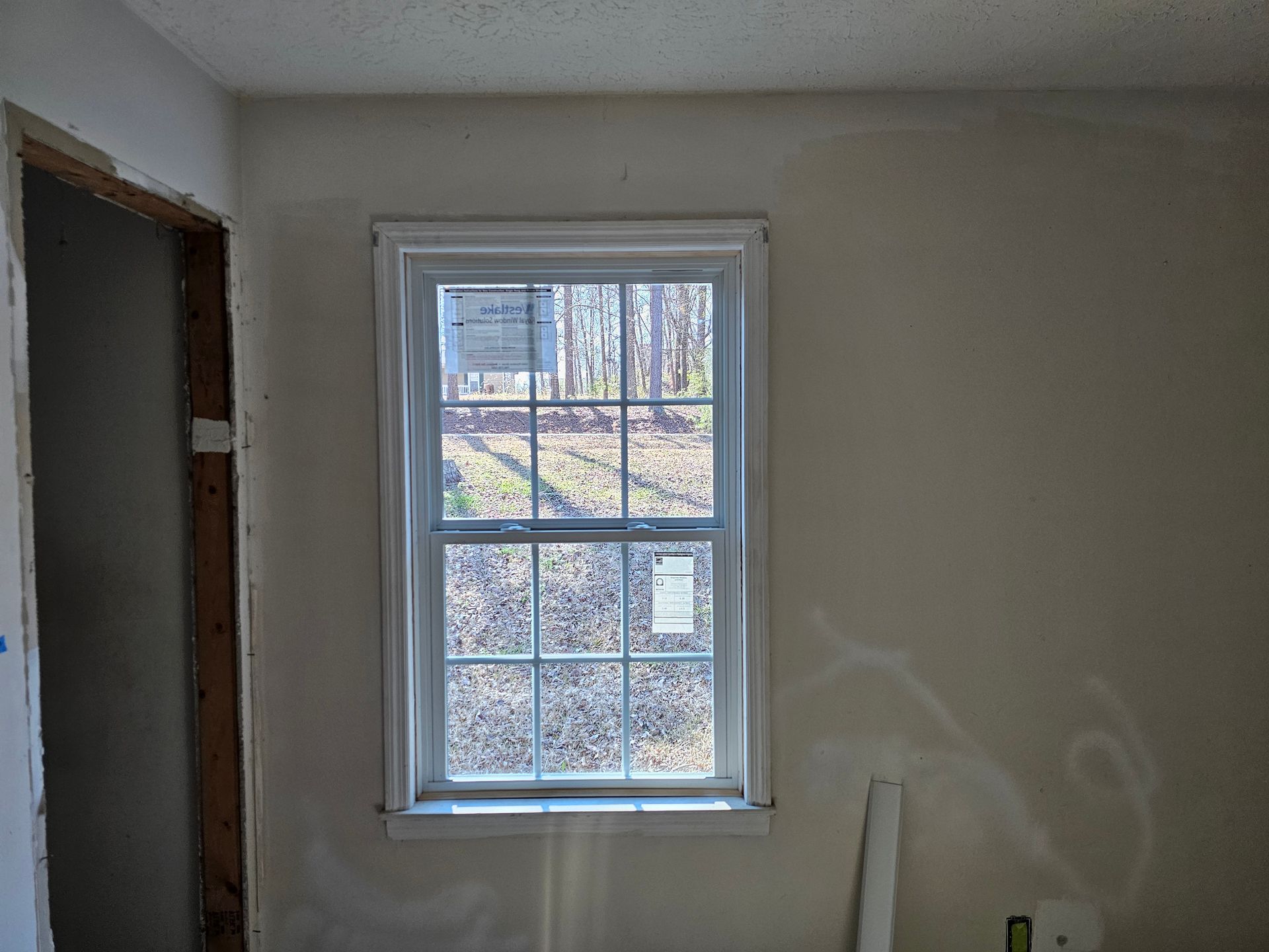 Window with white frame, set in off-white wall. Sunlight streams through glass, view of trees.