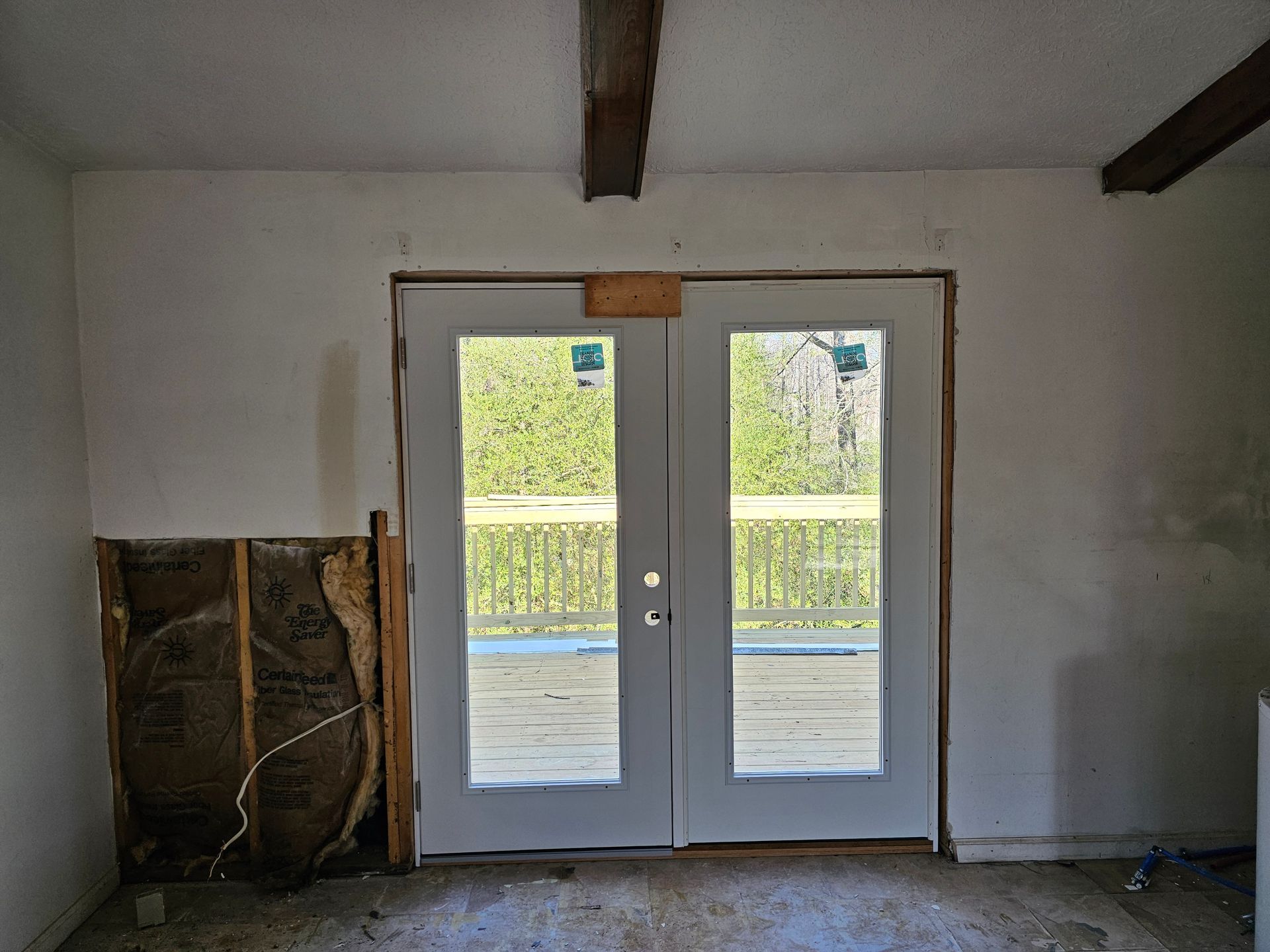Interior view of a room with unfinished walls, a doorway with double doors leading to a deck, and exposed insulation.