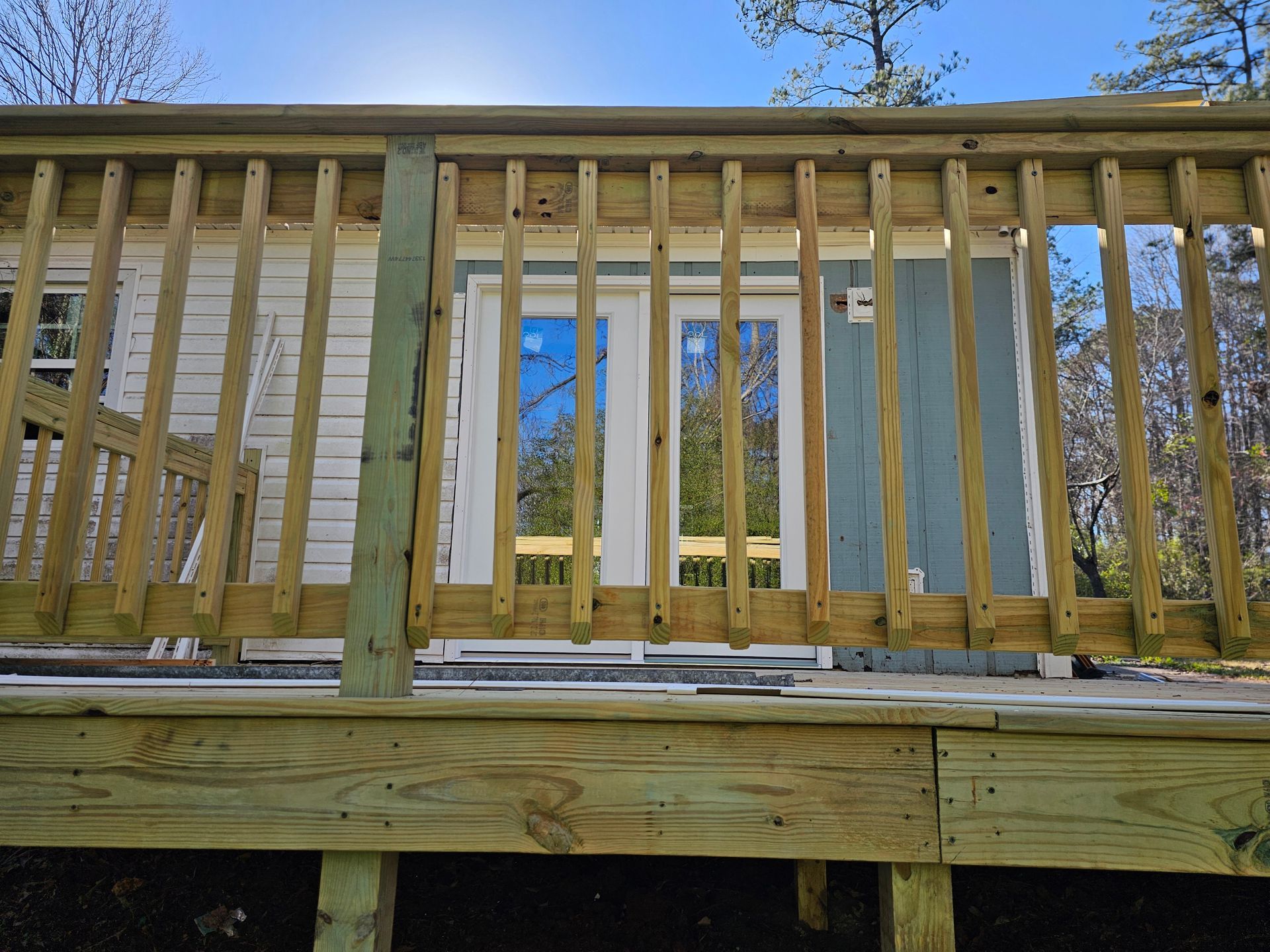 Wooden deck with railing overlooking a building with glass doors and blue siding.